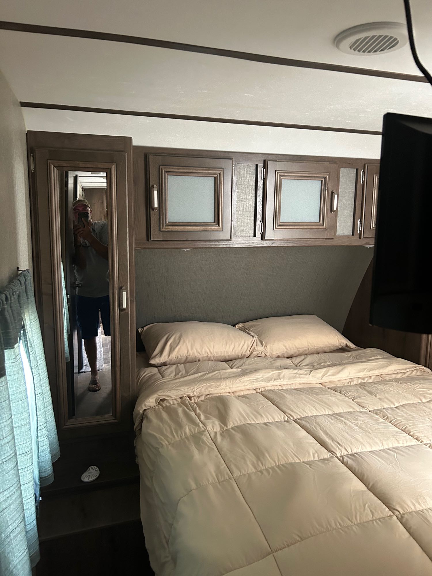 Comfortable RV rental bedroom featuring a cozy bed, overhead cabinets, and a full-length mirror.. Keystone RV Passport Grand Touring 2018
