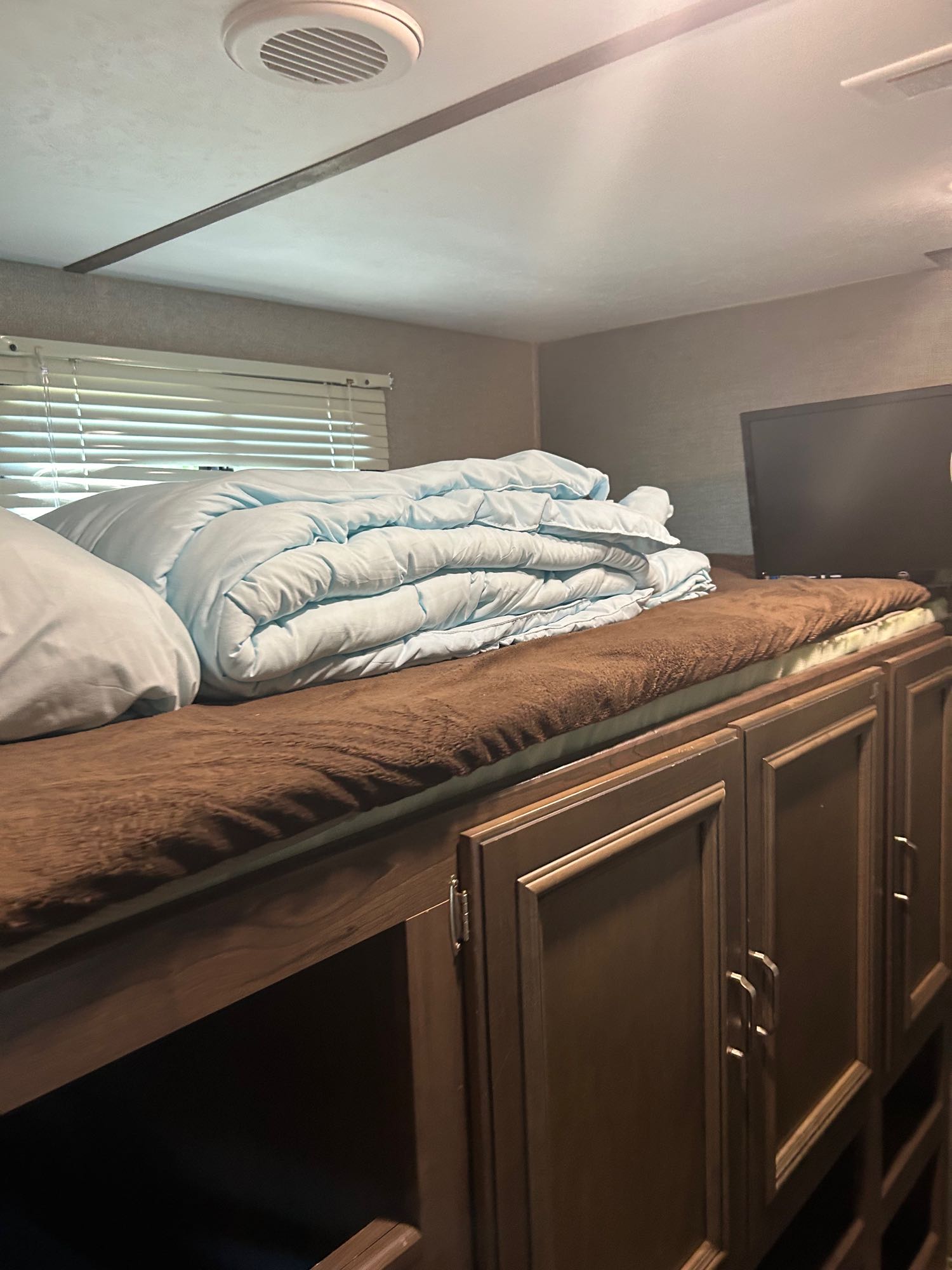 RV rental interior: A comfy bunk bed with light blue comforter, brown blanket, integrated cabinets, and TV.. Keystone RV Passport Grand Touring 2018