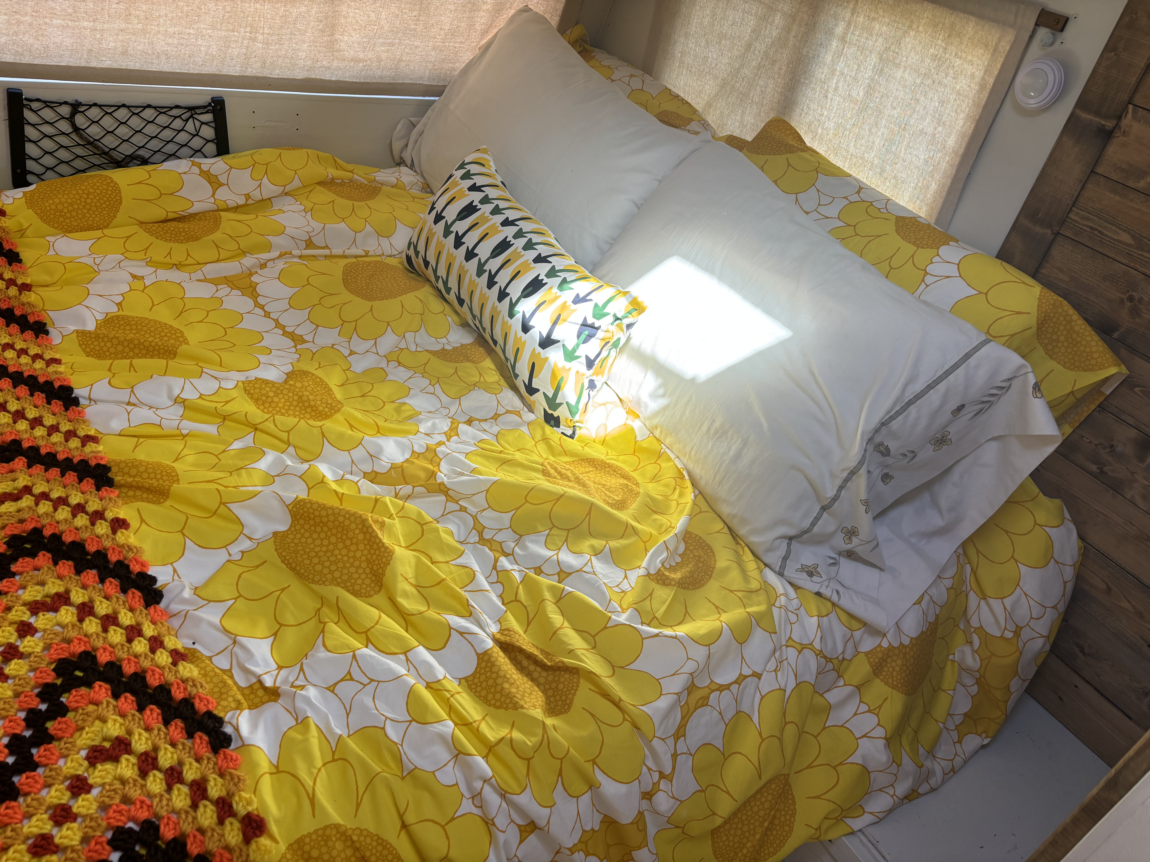 Bright & cozy RV rental bed with cheerful sunflower bedding, colorful crocheted blanket, and storage.. Vanguard Industries other 1972