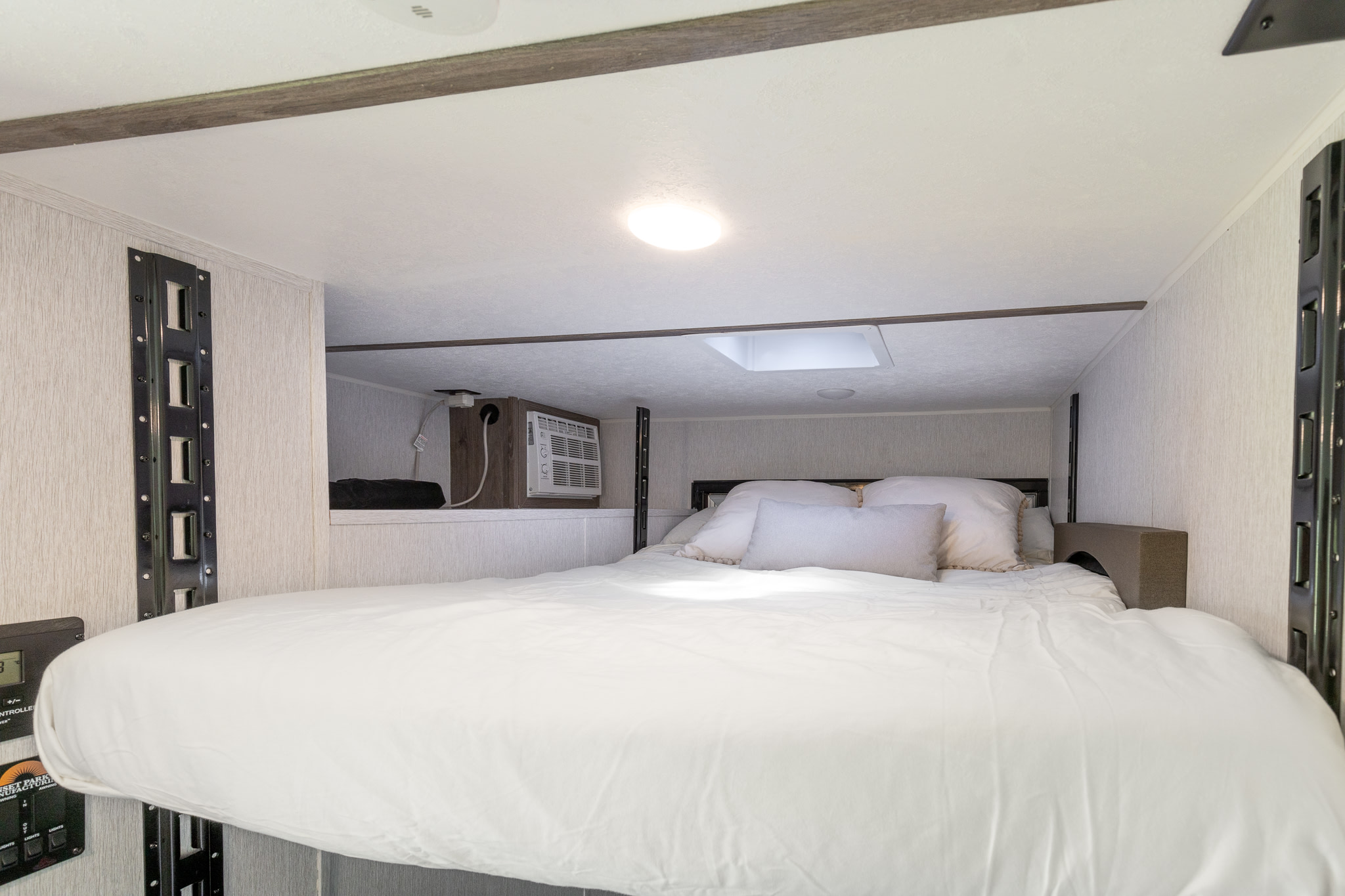 Experience comfort in this modern RV rental: a cozy loft bed, AC unit, and control panel define this compact living space.. Sunset Park & Rv Inc. sunray 139t 2024
