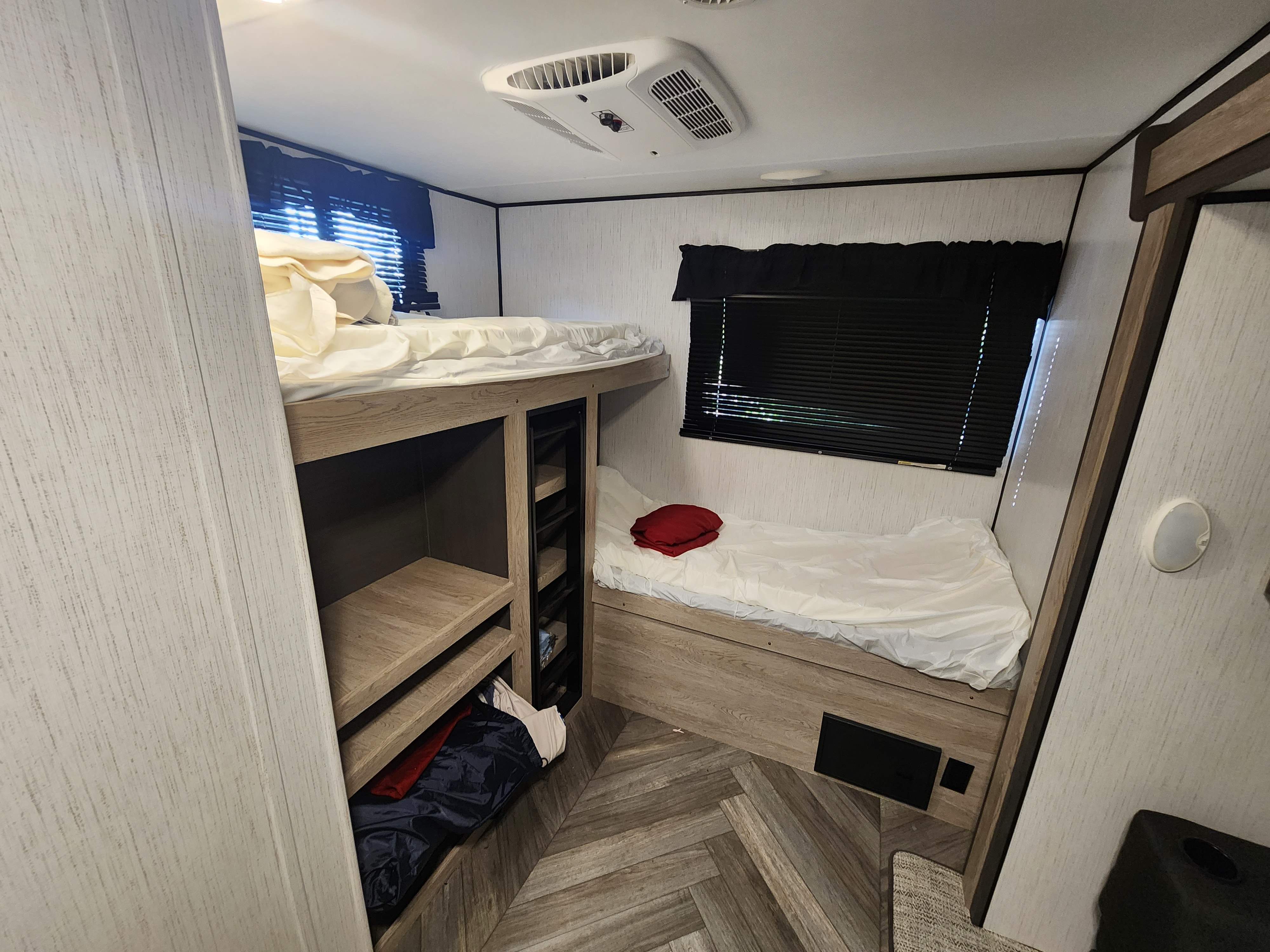 Inside an RV rental: a compact bunk bed sleeping area with storage shelves, ceiling AC, and wood-look flooring.. Heartland RVs Prowler 2022