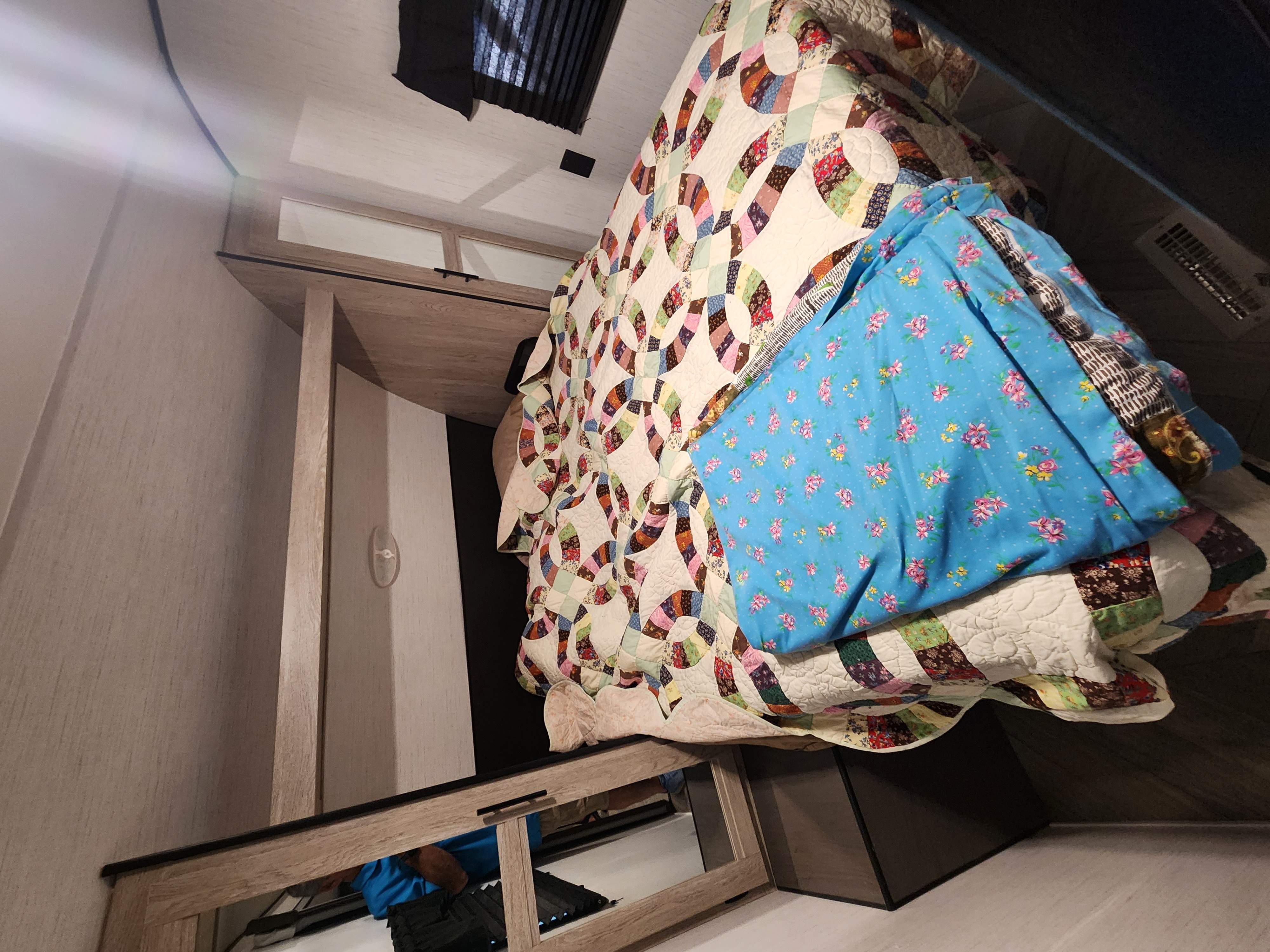 Cozy RV rental bedroom featuring a bed with vibrant patterned quilts. Light wood built-in storage and overhead vent visible.. Heartland RVs Prowler 2022