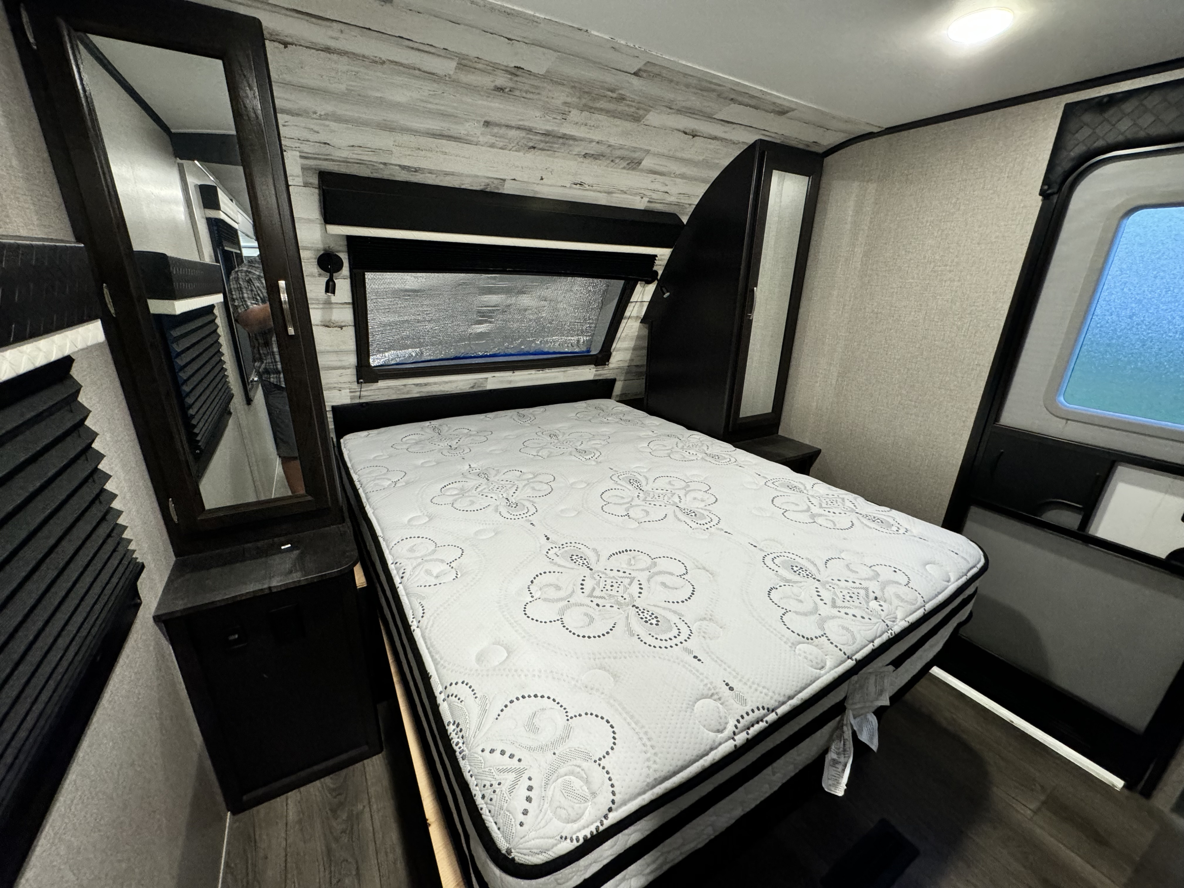 Spacious RV rental bedroom with queen mattress, dark wood cabinets, mirrors, window, and wood-look flooring.. Jayco White Hawk 2020