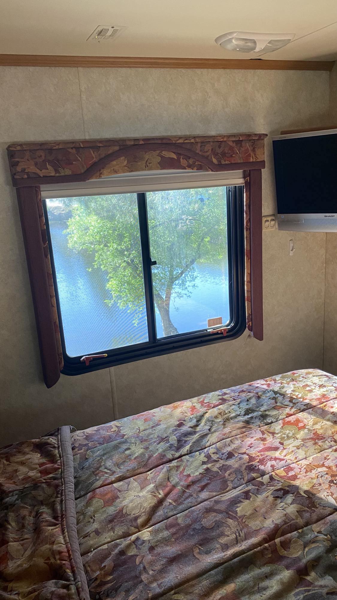 Step inside this cozy RV rental bedroom. Enjoy the serene window view of a tree by the water, ideal for travel getaways.. Holiday Rambler Neptune 2008
