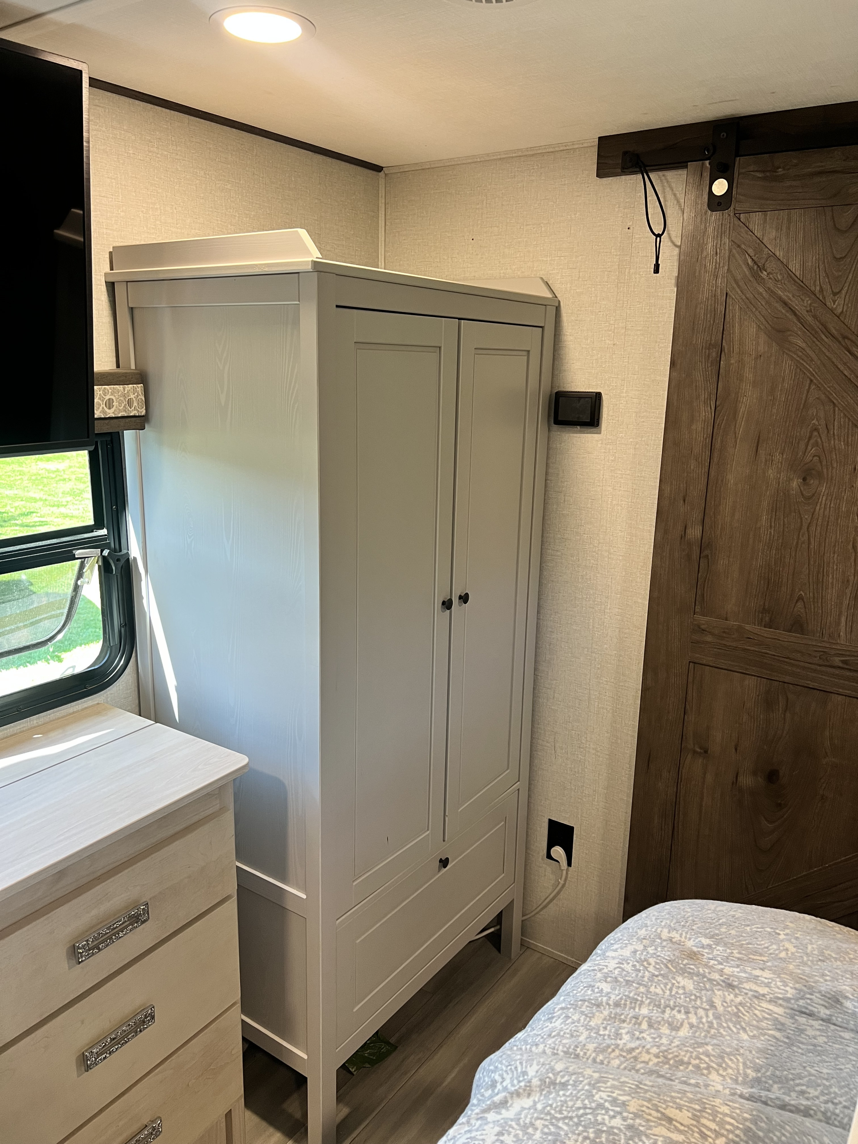 RV rental bedroom with a light gray wardrobe, dresser, window, TV, and sliding barn door inside.. Alliance RV Paradigm 2021