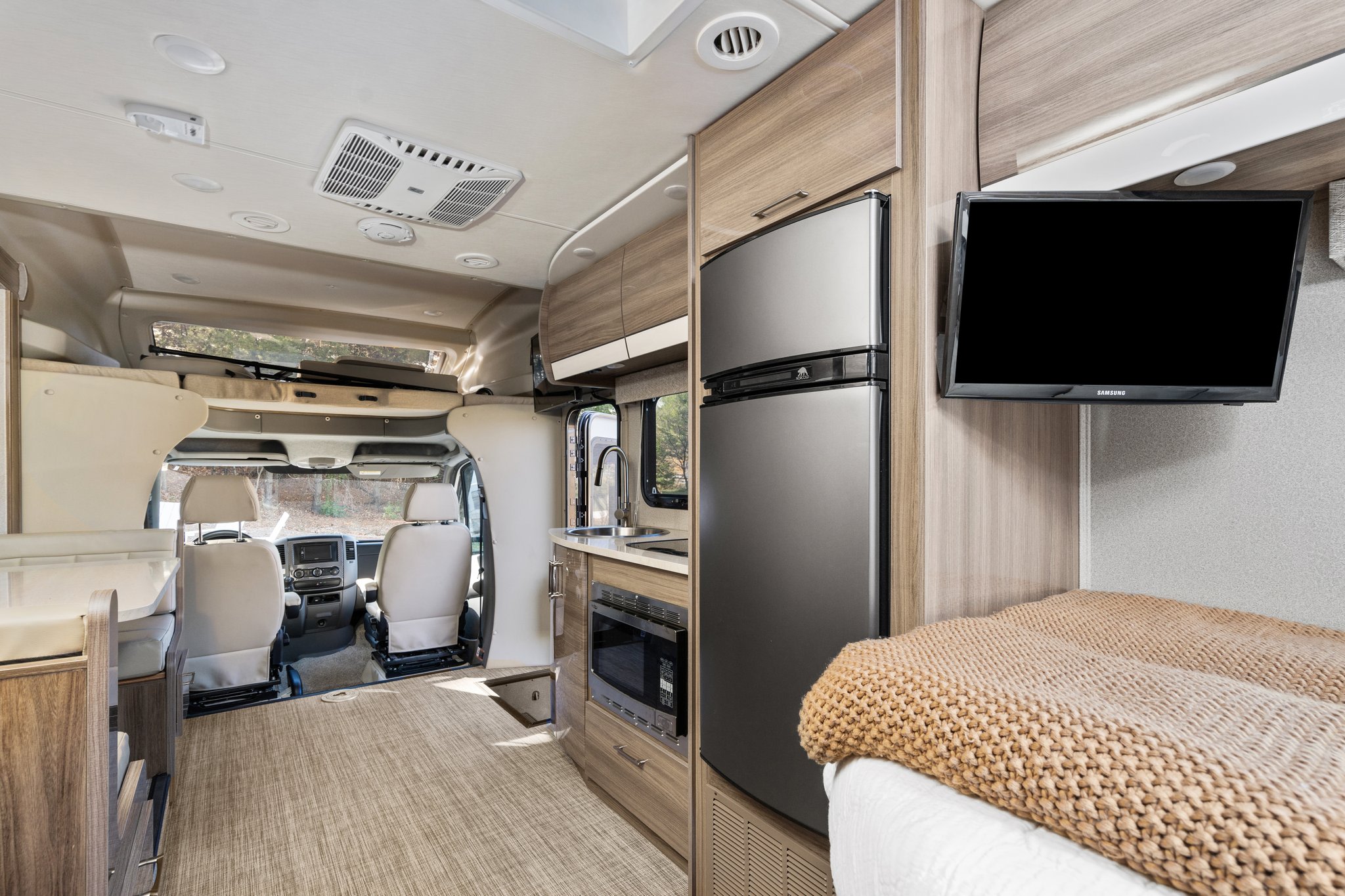Explore this modern RV rental interior featuring a well-equipped kitchen, comfortable sleeping area with TV, and spacious front cockpit.. Entegra Coach Qwest 2018