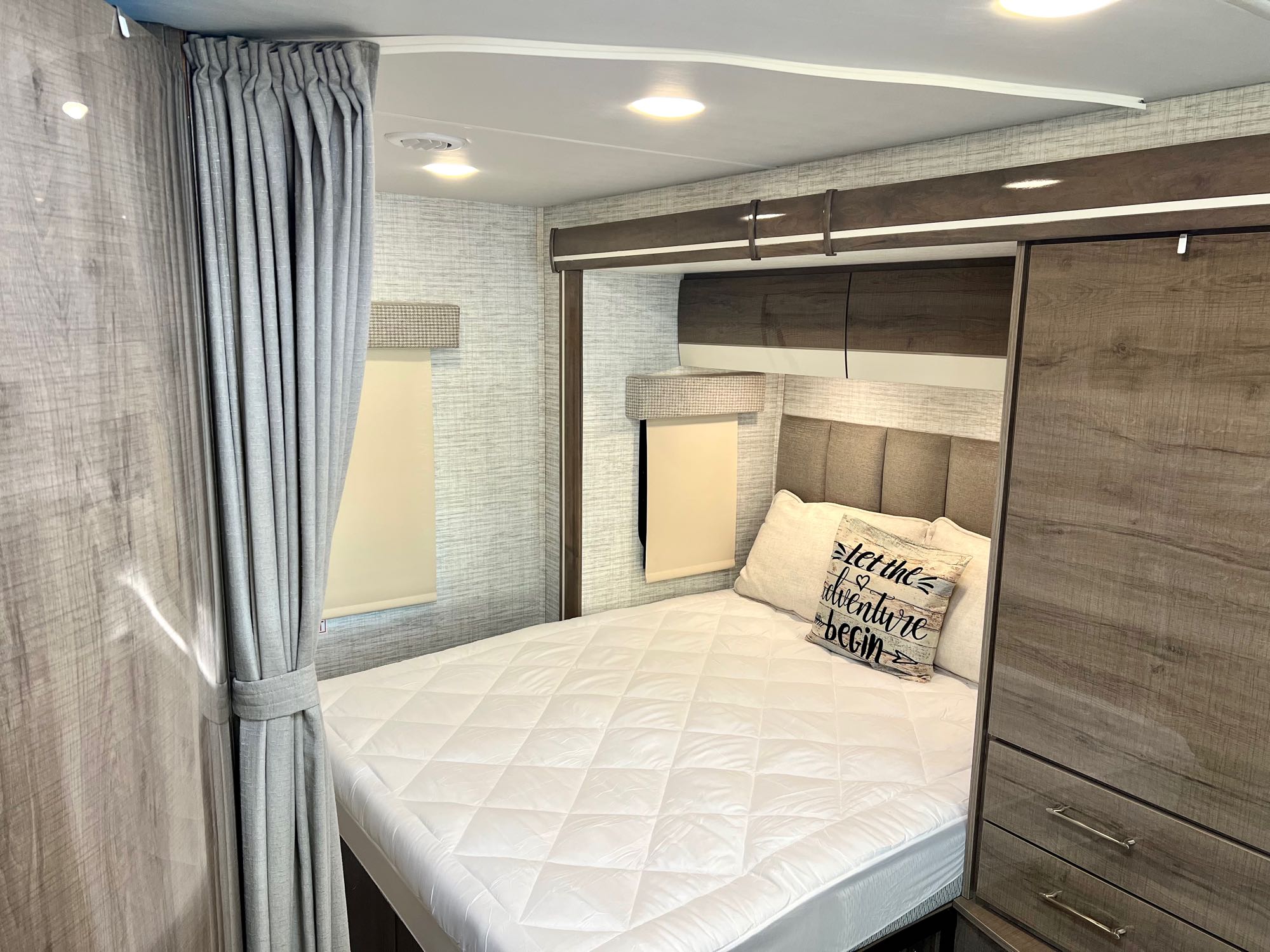 This RV rental bedroom features a comfortable bed with quilted mattress, wood-grain storage, and neutral tones.. Entegra Coach Qwest 2024