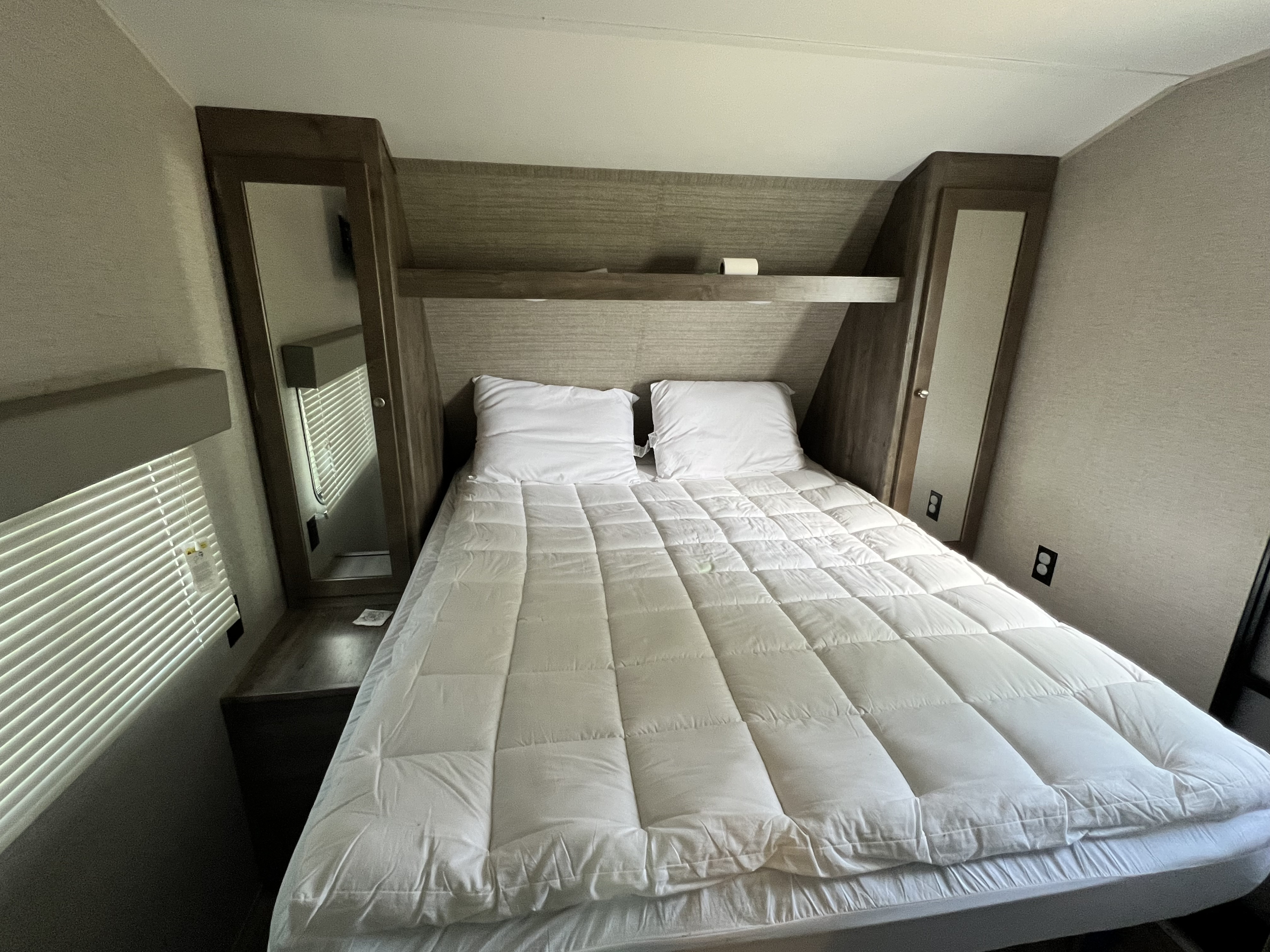 Cozy RV rental bedroom with a queen bed, white comforter, pillows, built-in mirrored wardrobes, and an overhead shelf.. Aspen Trail Aspen Trail Trailer 2019