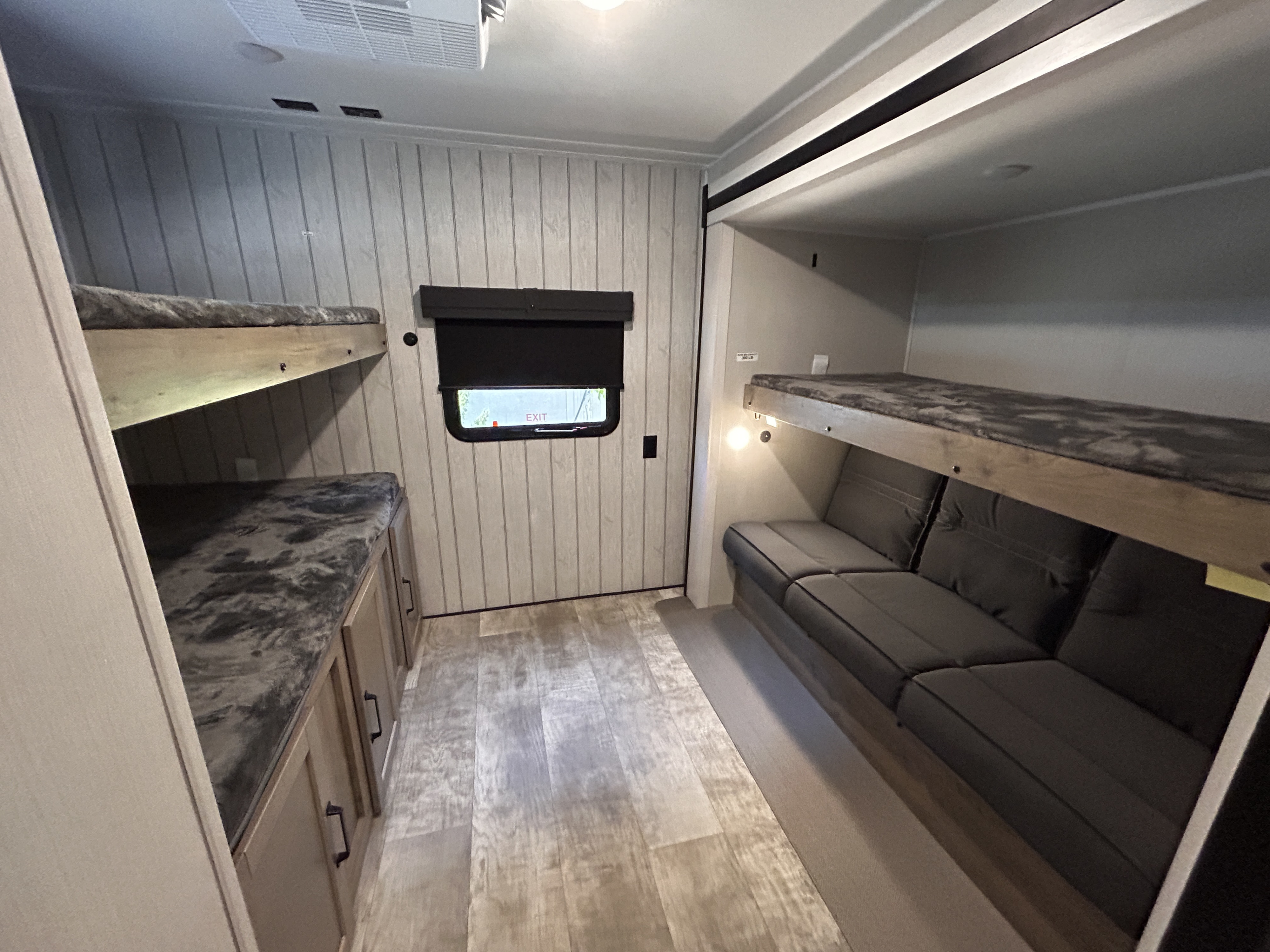 RV rental bunkhouse: Left wall features a top bunk above storage cabinets. Right wall has a top bunk over a sofa. Window visible.. Palomino Puma 2024