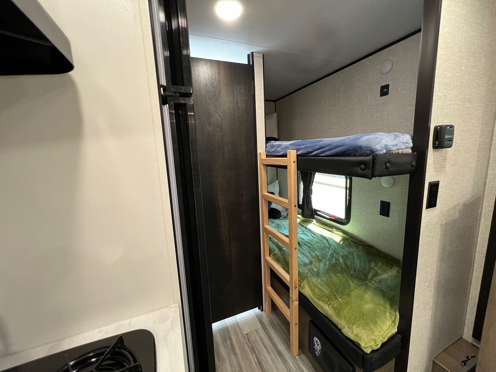 RV rental interior: bunk beds with ladder and blankets. Left shows part of a kitchen with a stove burner.. Jayco Jay Flight SLX Baja Edition 2024