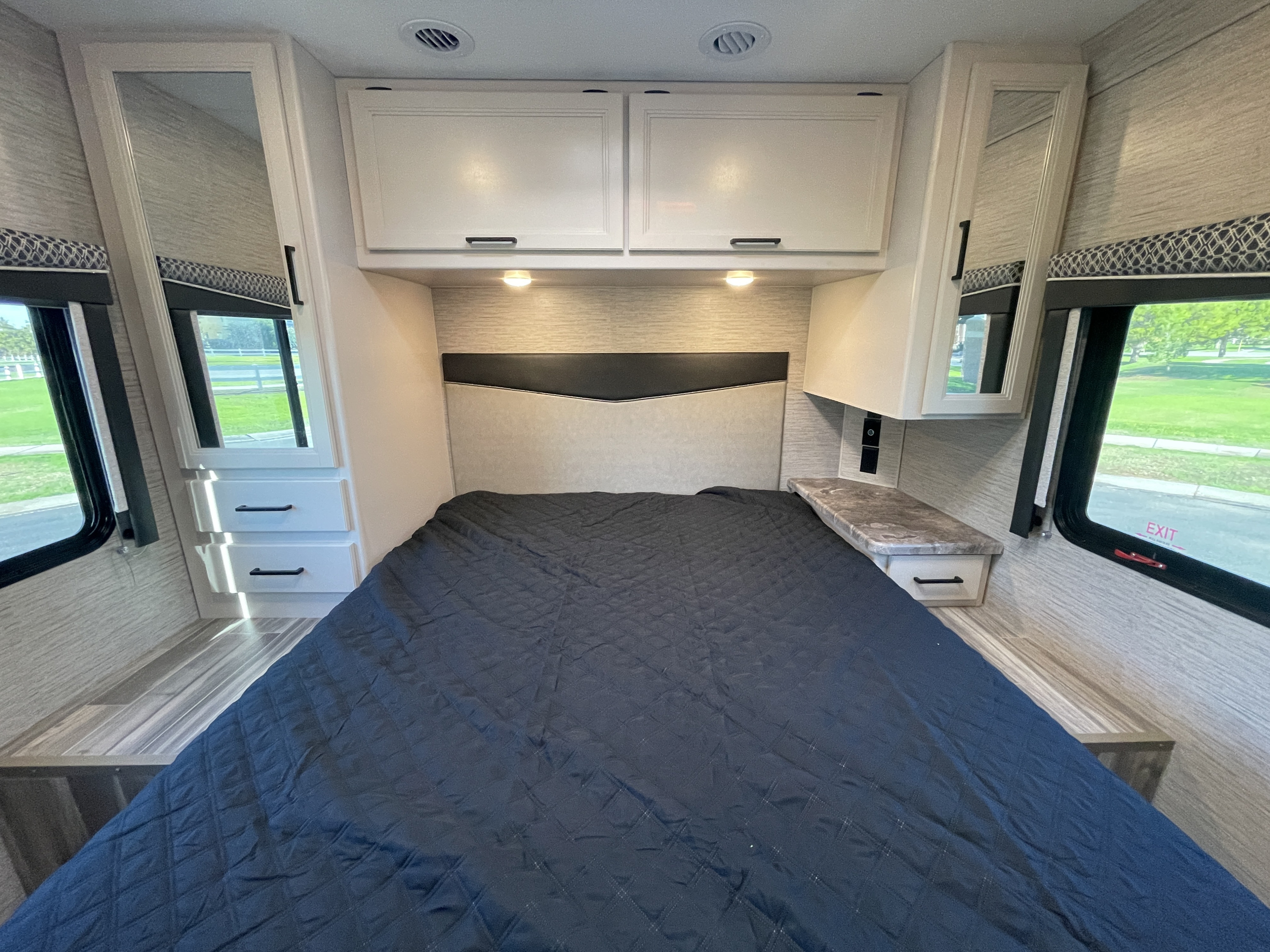 Comfortable RV rental bedroom: large bed, white overhead cabinets, side storage, and windows showcasing outdoor views.. Thor Motor Coach Four Winds 2023