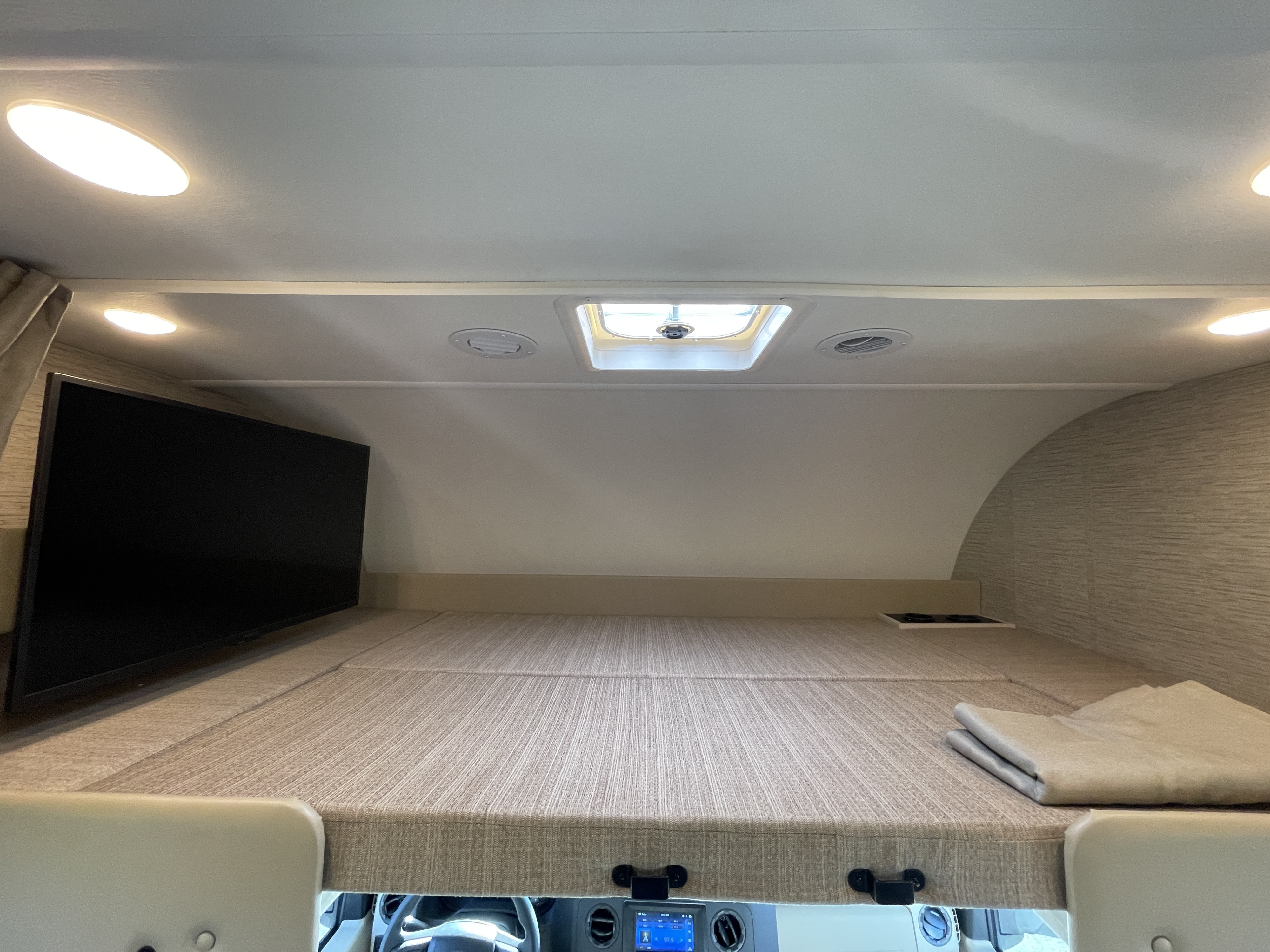 RV rental cab-over bunk: a cozy bed with a TV, skylight, and ceiling vents. A comfortable sleeping area.. Thor Motor Coach Four Winds 2023