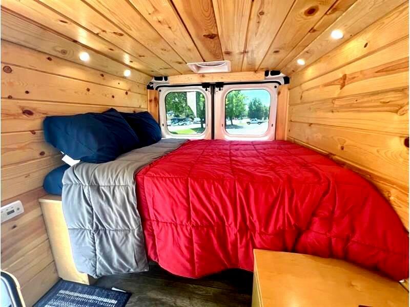 This RV rental offers a compact, cozy interior with warm wood paneling, a comfy bed, and views out the back windows.. Dodge Sprinter Van 2019