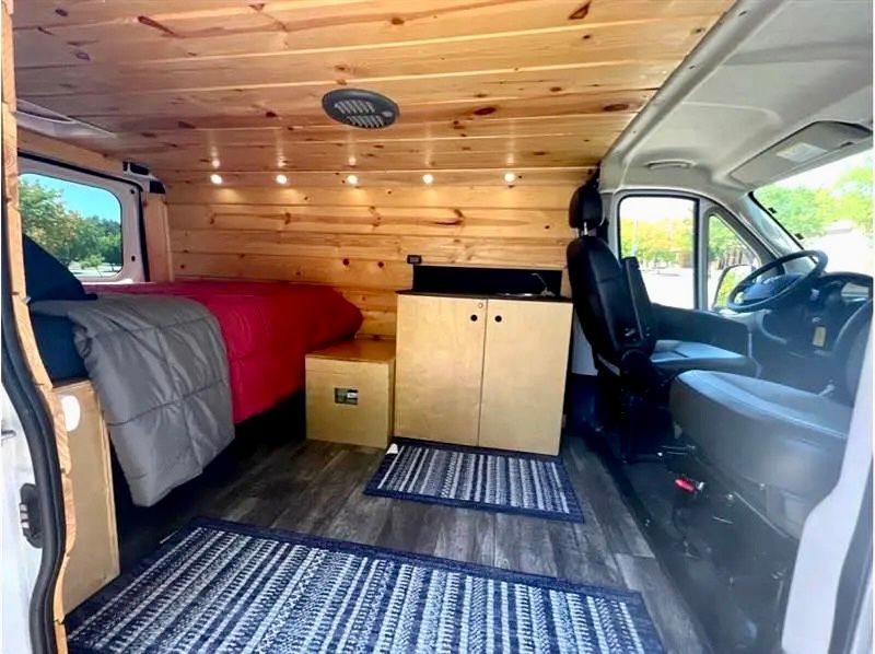 Spacious custom RV rental interior with bed, kitchen, wood paneling, and comfortable seating. Perfect for road trips.. Dodge Sprinter Van 2019