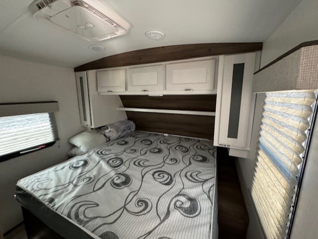 Inside an RV rental bedroom: features a patterned bed, overhead cabinets, and windows with blinds.. Cruiser RV MPG Ultra Lite 2024