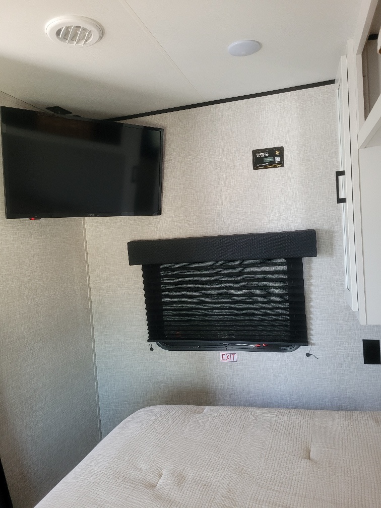 Cozy RV rental bedroom showing a wall-mounted TV, shaded window with 'EXIT' sign, and comfortable bed for your travels.. Jayco Jay Flight SLX 2024