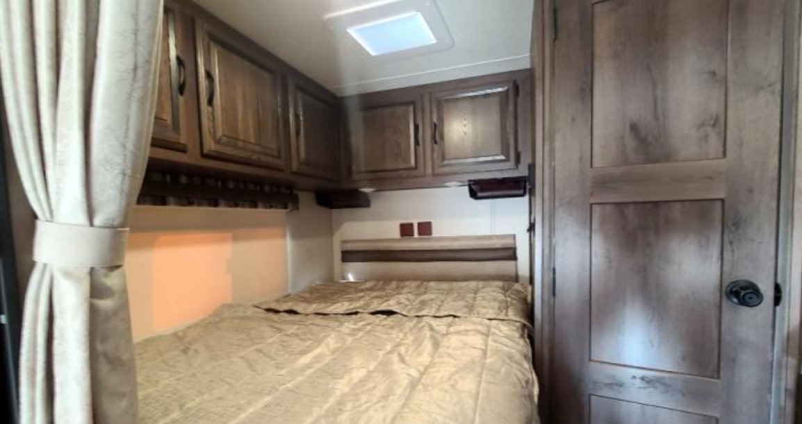 RV rental bedroom: A cozy space with a beige bed, wooden cabinets, and a skylight.. Coachmen Prism 2150 2019