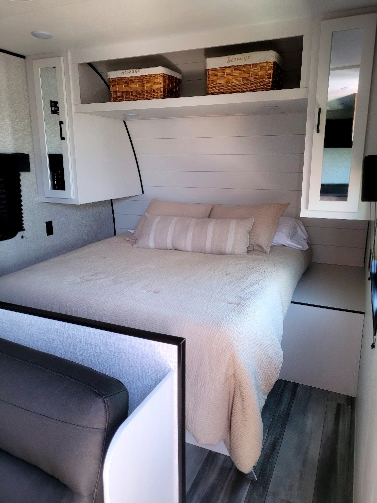 Cozy RV rental bedroom: queen bed with pillows, shiplap headboard, and overhead storage cabinets with mirrors.. Jayco Jay Flight SLX 2024