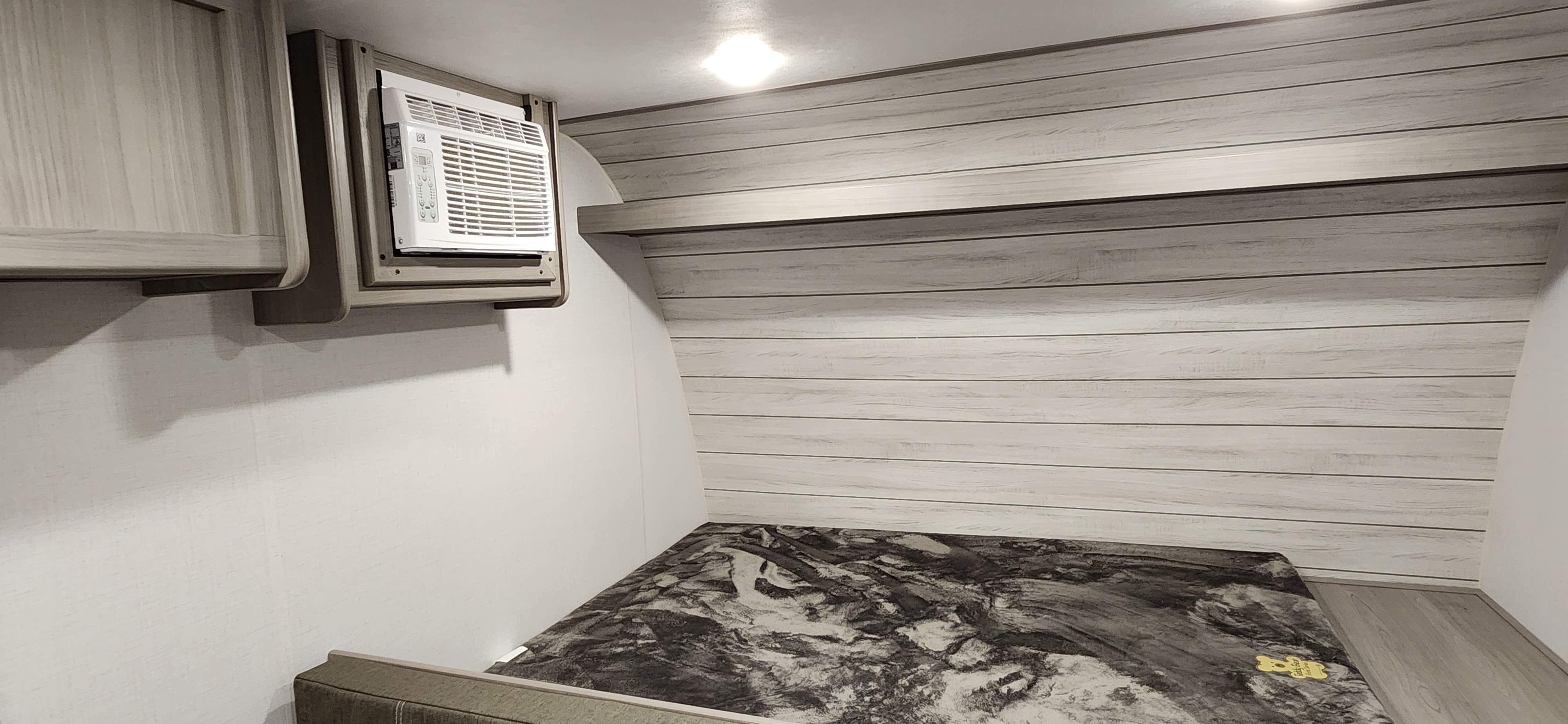 Cozy RV rental interior: bedroom with a modern AC unit, patterned bed, light wood walls & cabinets.. coleman Coleman Lantern LT 17B 2024