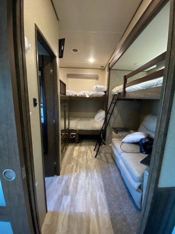 This RV rental's bunkhouse area features a comfy sofa and multiple beds, ideal interior for family travel trailer adventures.. Grand Design Solitude 2020