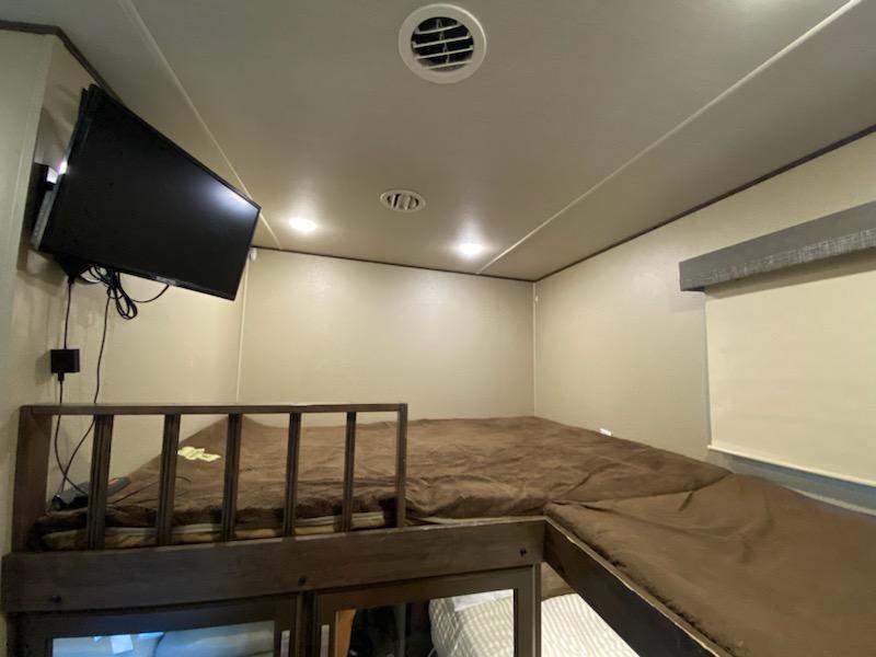 RV rental interior showing comfortable L-shaped bunk beds with brown bedding, wall-mounted TV, and window.. Grand Design Solitude 2020