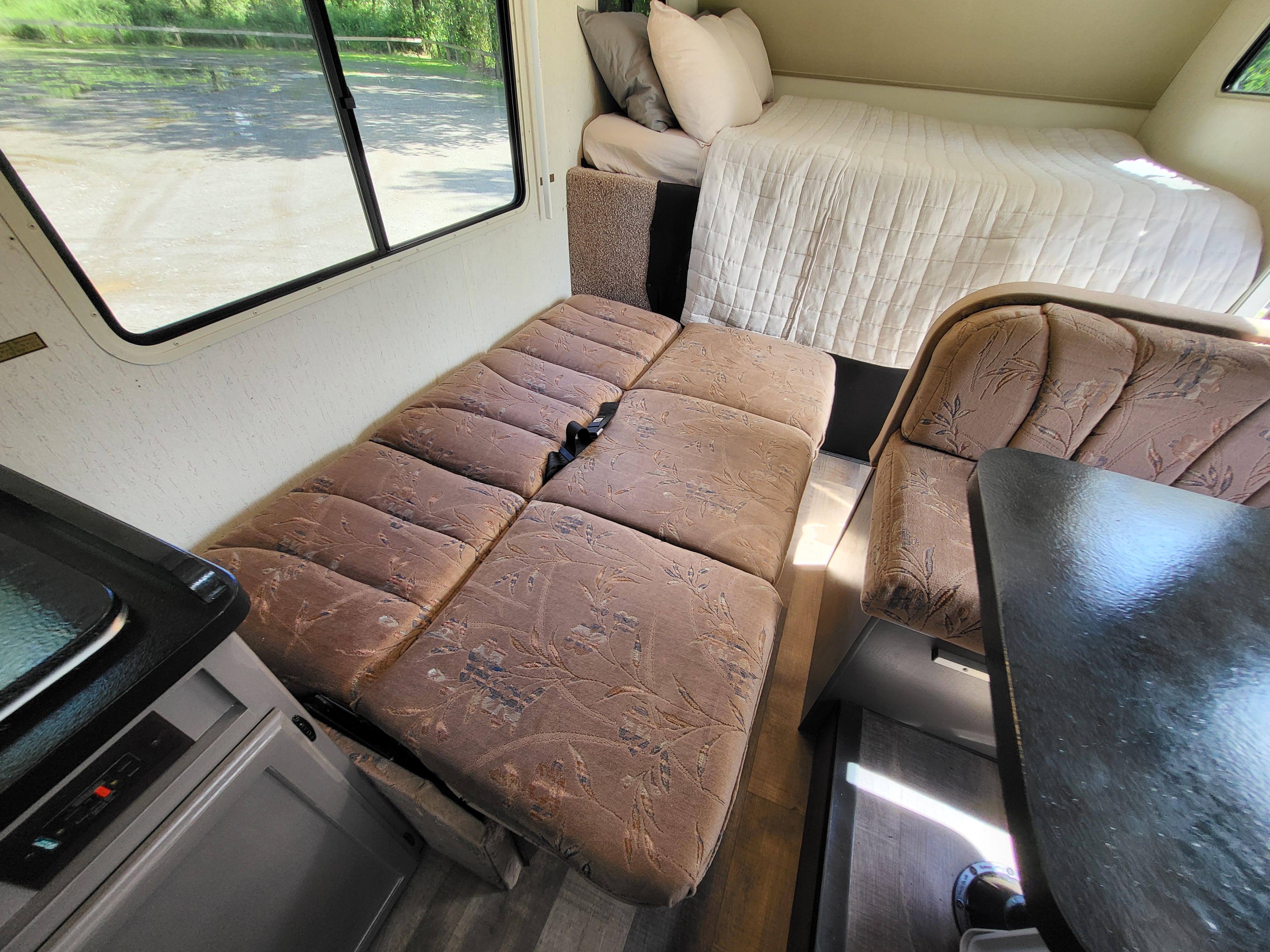 RV rental interior: Cozy bed, patterned convertible dinette, and kitchenette. Perfect for your road trip comfort.. Winnebago Warrior 1992