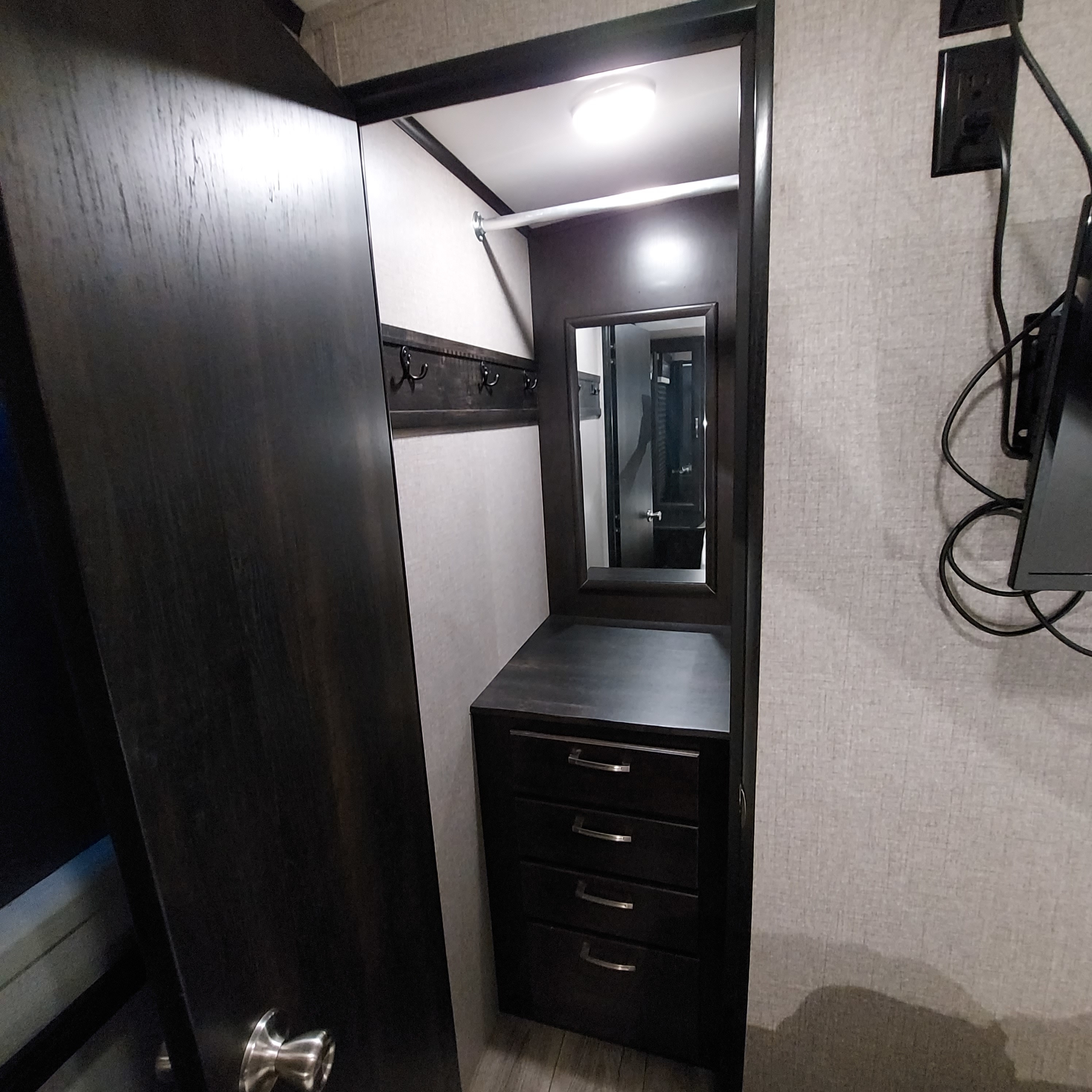 Compact RV rental wardrobe: Dark wood closet with hanging rod, mirror, and drawers provides smart storage for your travels.. Jayco White Hawk 2021