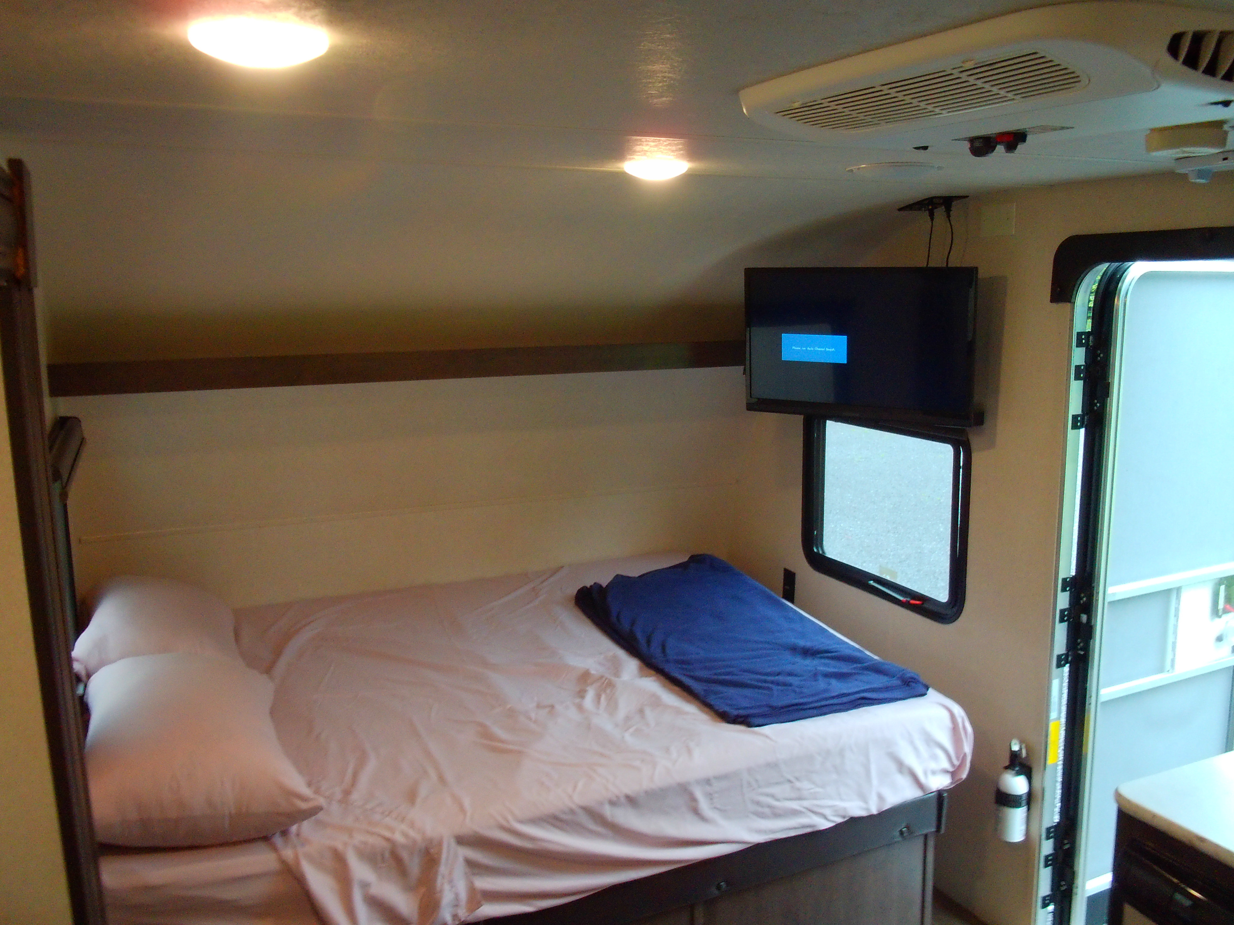Inside an RV rental, showing the compact bedroom area with bed, TV, AC unit, and a fire extinguisher.. Forest River Wildwood FSX 2018