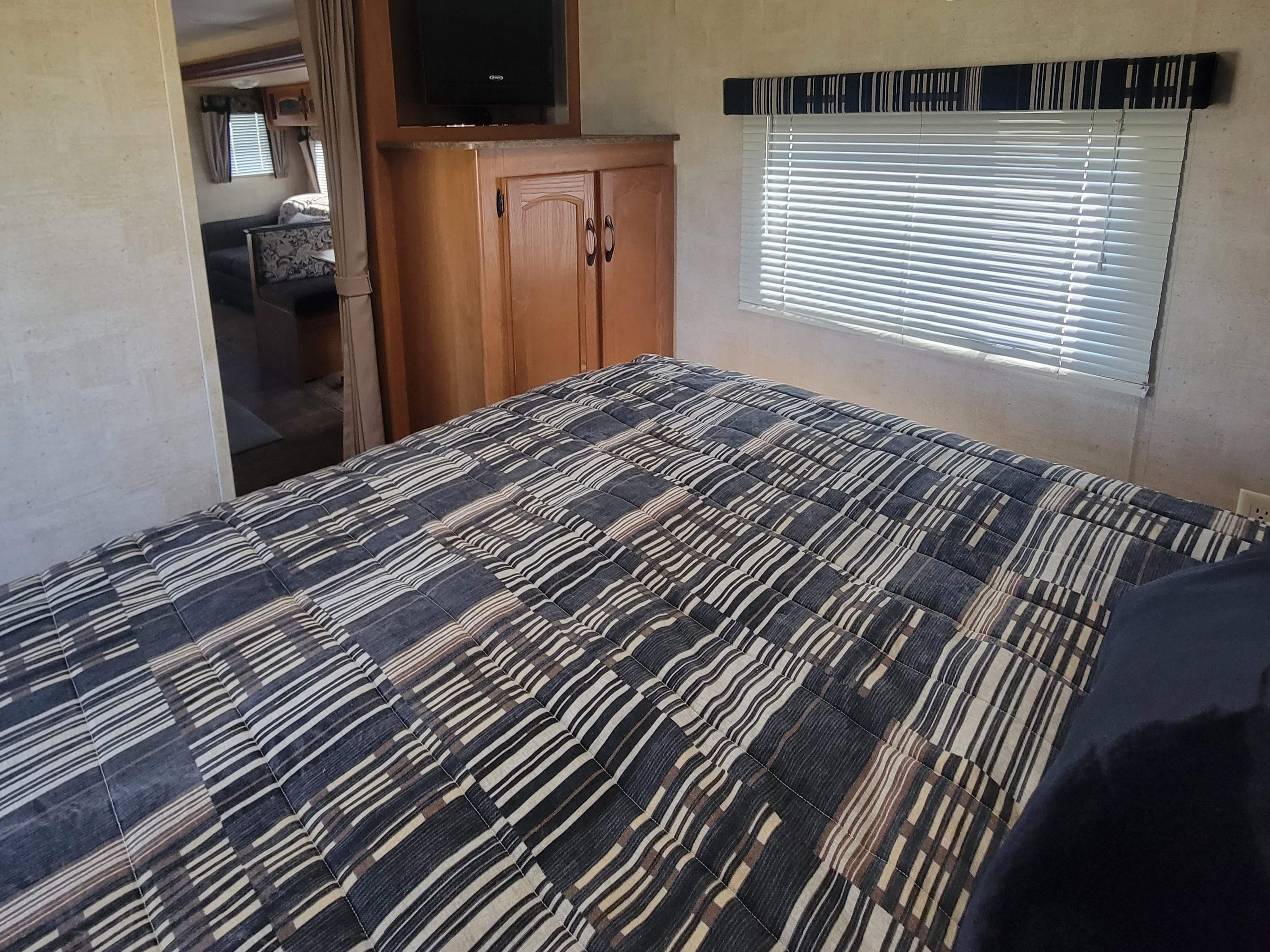 RV rental bedroom featuring a patterned bed, storage cabinet with TV, and natural light from the window.. Keystone RV Outback 2011