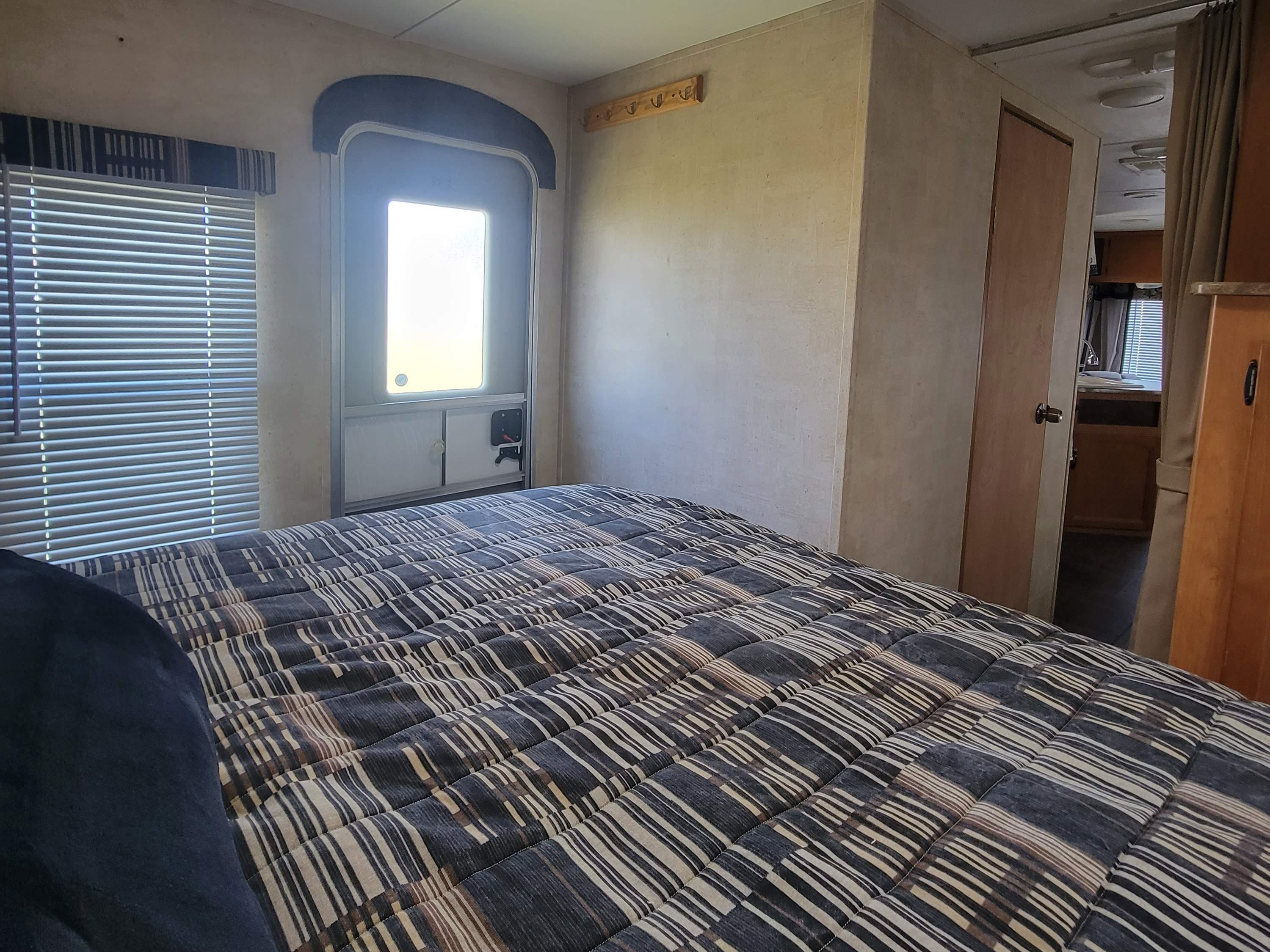 Cozy RV rental bedroom with striped bed, window blinds, and main entry door, perfect for your next adventure.. Keystone RV Outback 2011