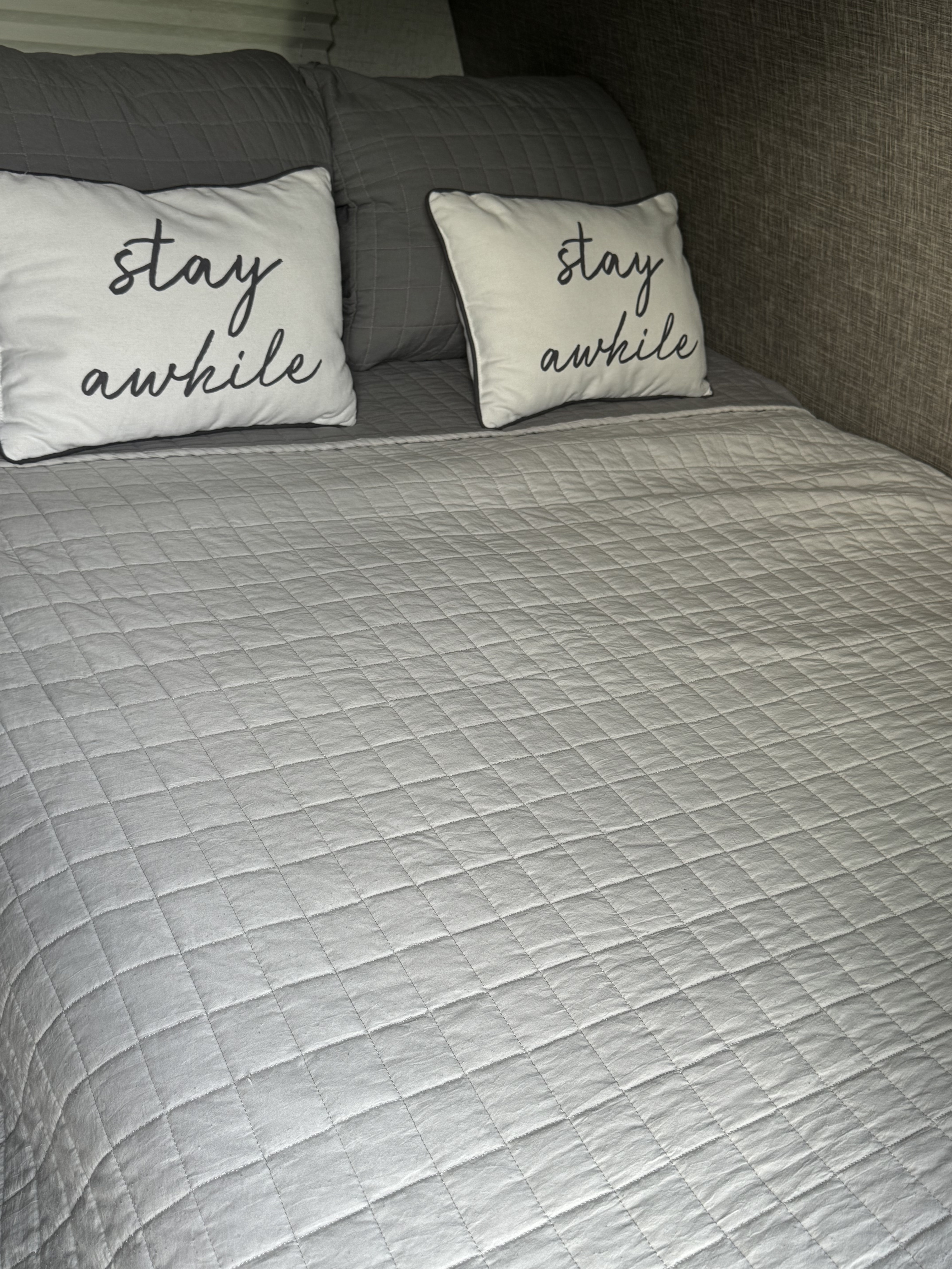 A comfortable gray quilted bed in an RV rental, featuring two white "stay awhile" pillows.. Winnebago Industries Towables 1800bh 2022