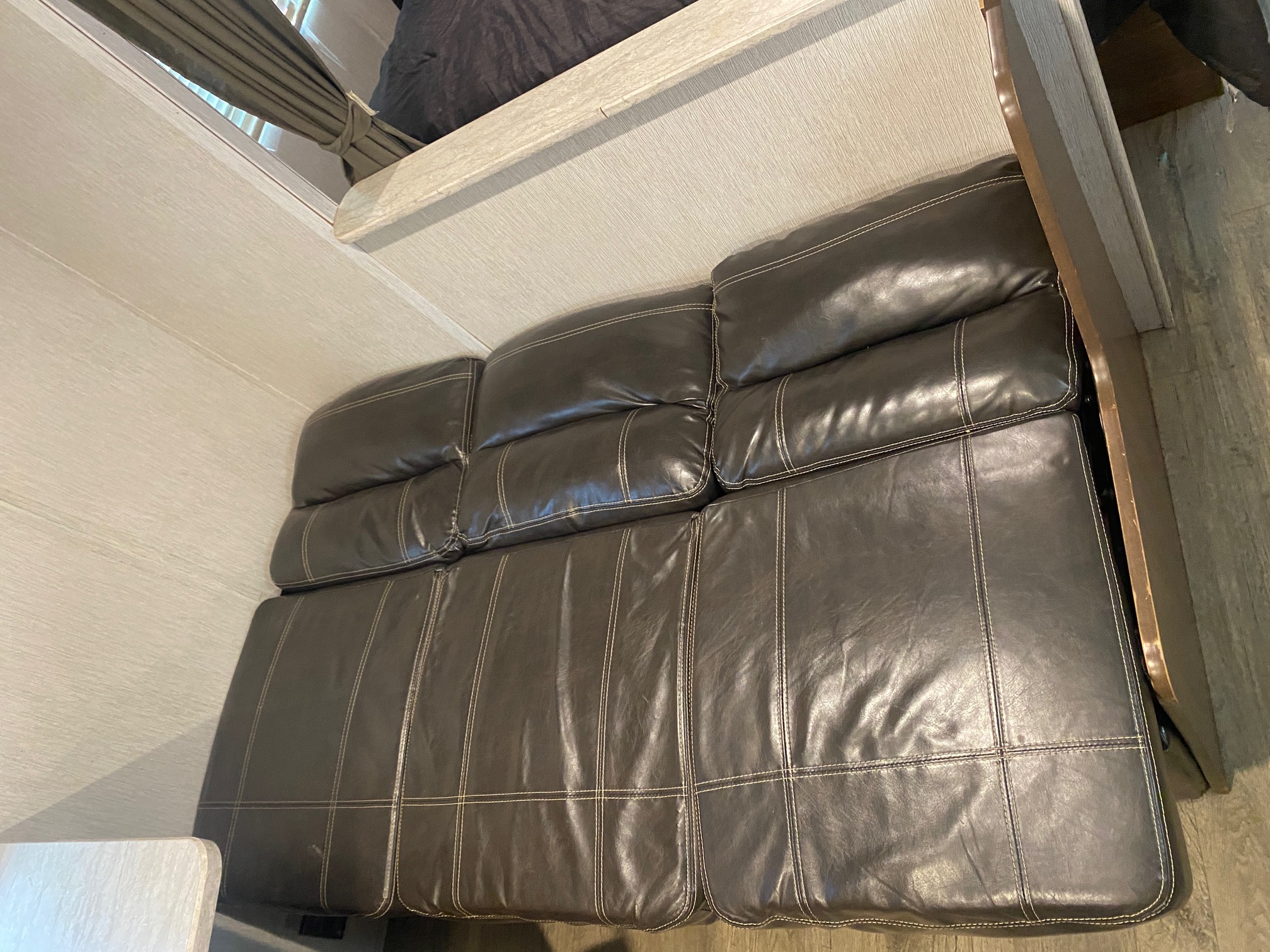 Relax on the dark leather sofa inside this RV rental, featuring an overhead bunk bed, window with curtain, and wood flooring.. Heartland RVs Prowler Lynx 2019