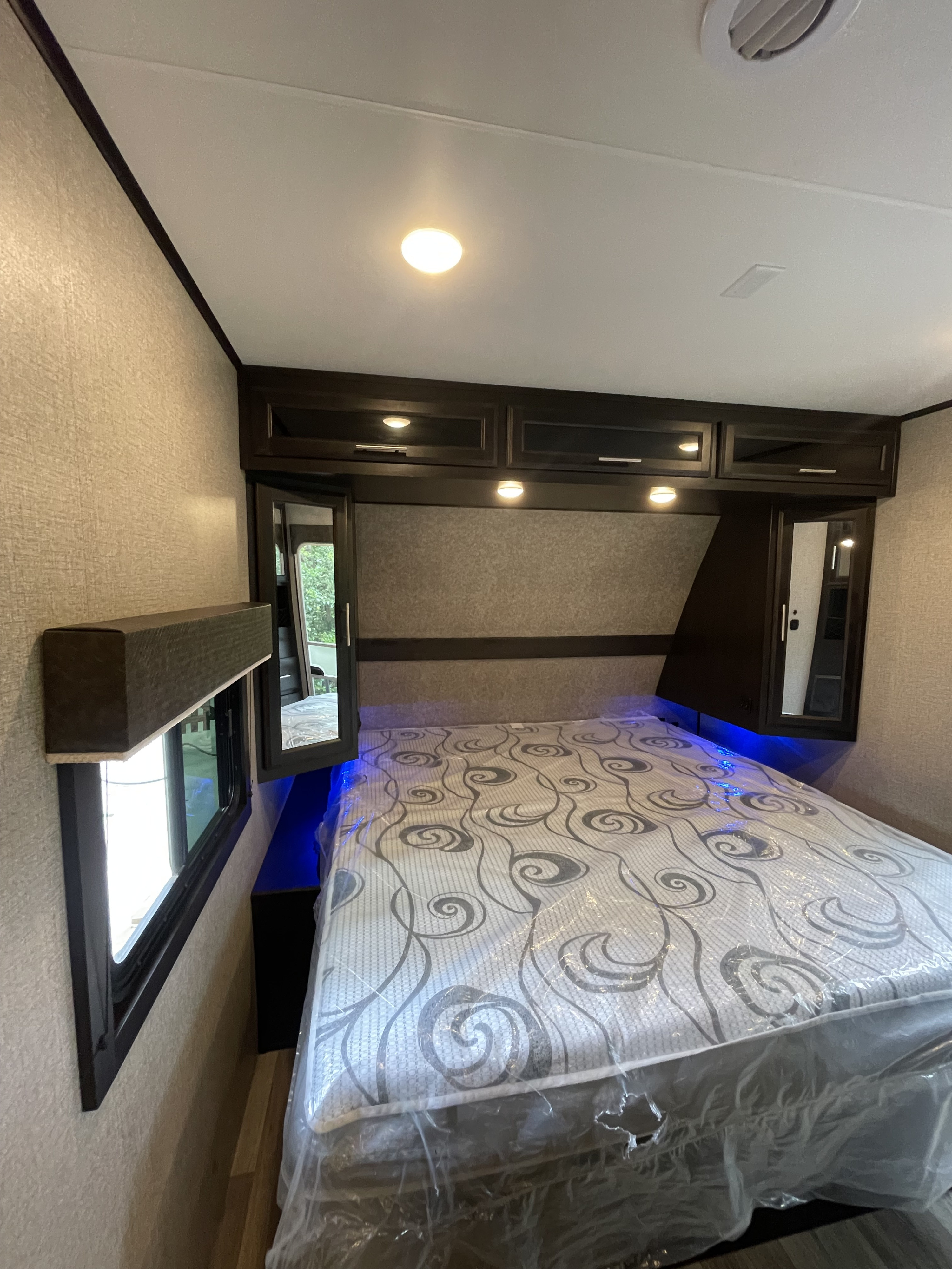 Modern RV rental bedroom: bed in plastic, overhead cabinets, and blue accent lights illuminate the bed.. Jayco Eagle 2021
