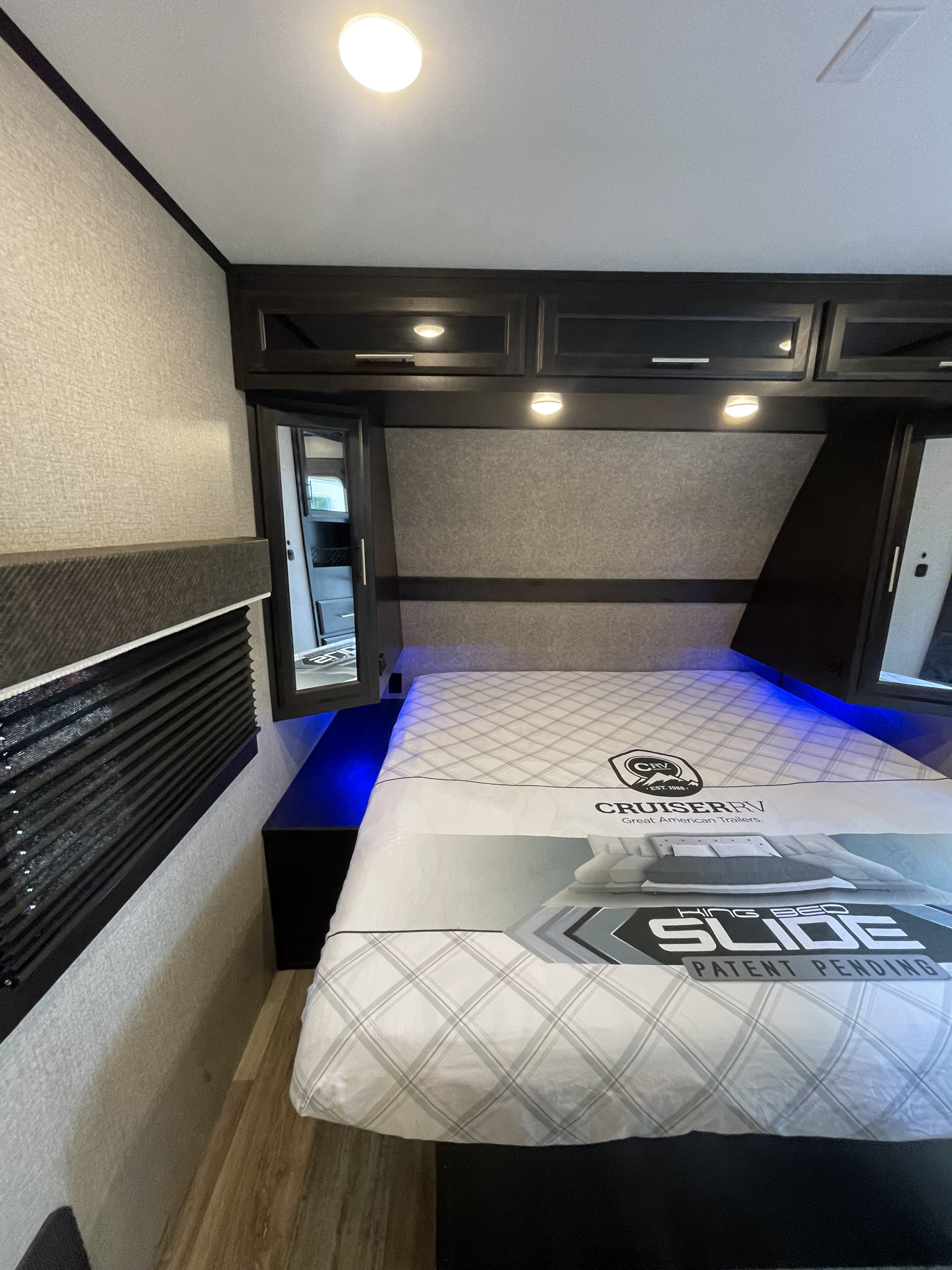 Spacious RV rental bedroom with a King Bed Slide, overhead cabinets, and cozy blue lighting. Perfect for your next adventure!. Jayco Eagle 2021