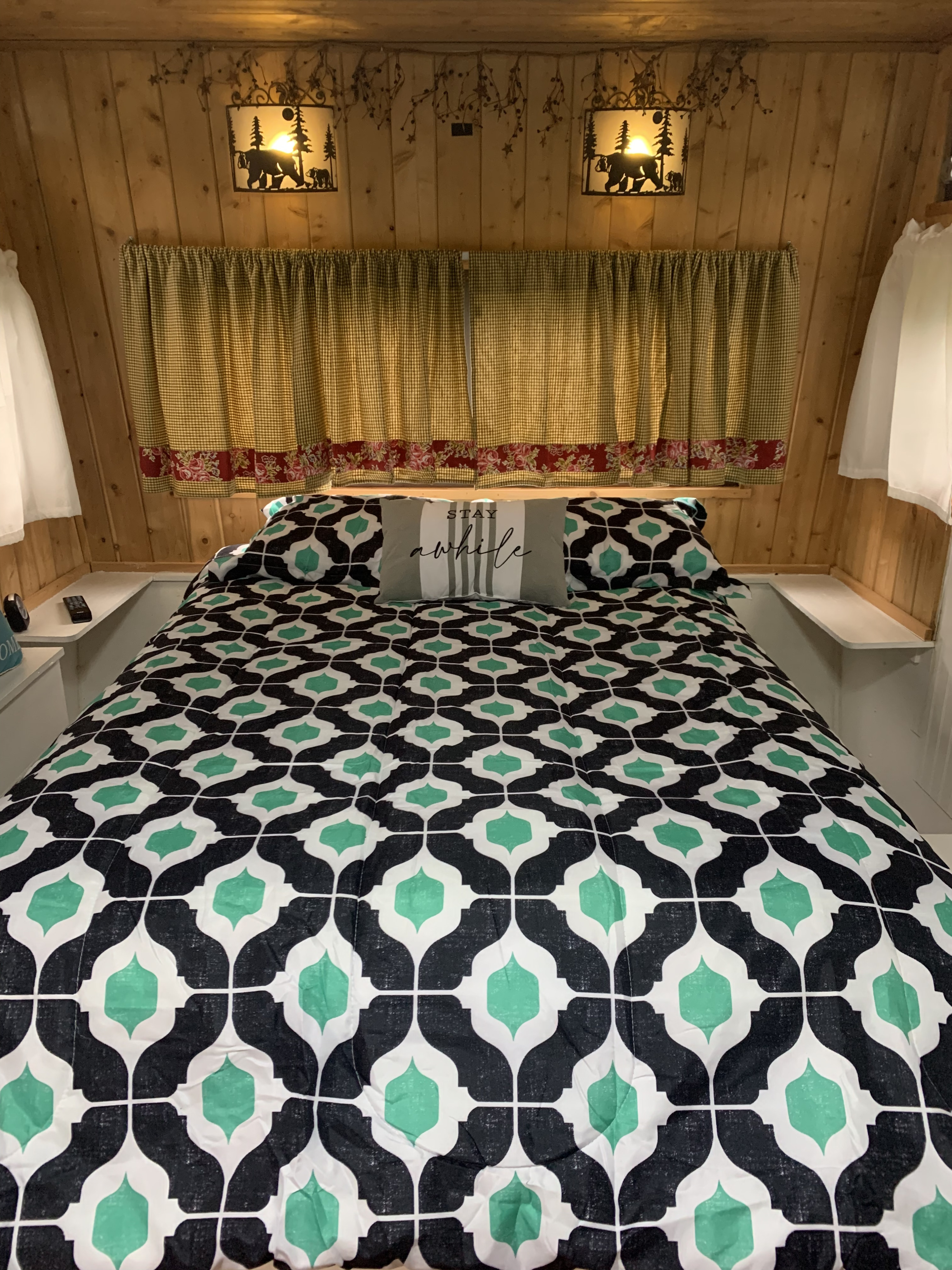Cozy RV rental bedroom features a patterned comforter, rustic bear wall lights, and wooden paneling for a warm escape.. Serro Scotty Sportsman 1984