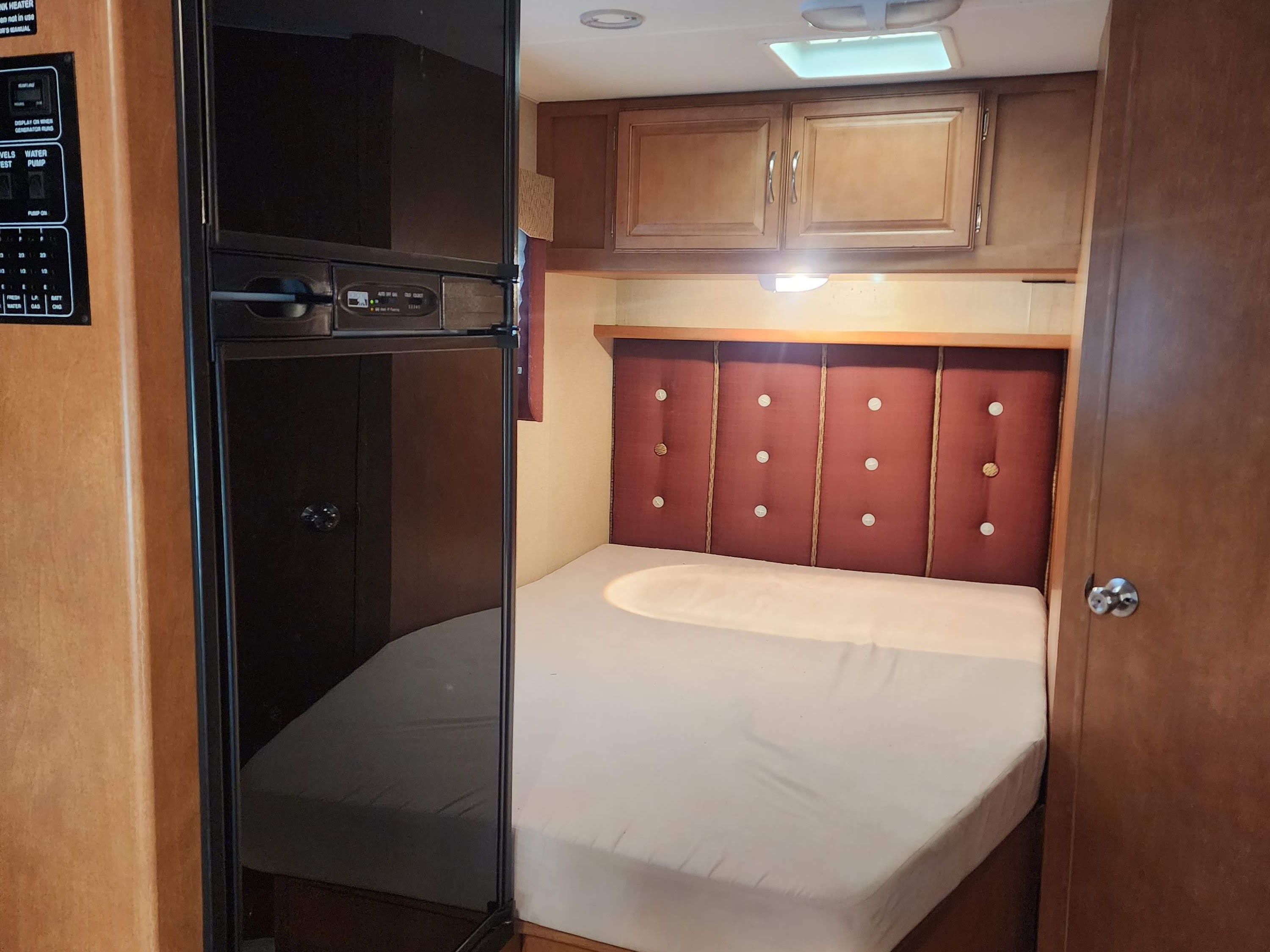 RV rental interior showcasing a cozy bedroom with a bed, upholstered headboard, overhead cabinets, and a side refrigerator/control panel.. Itasca Spirit 2015