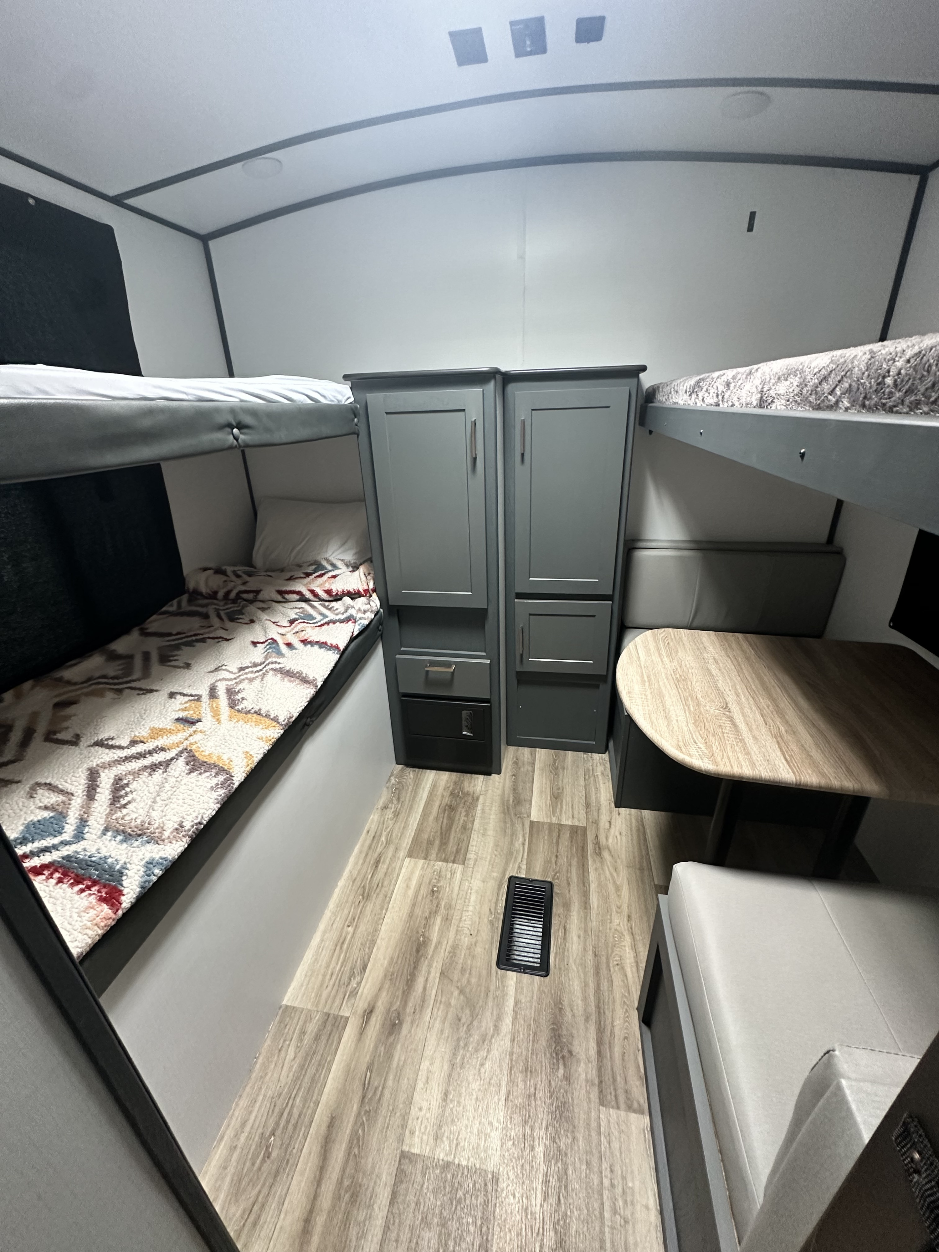 This RV rental interior features bunk beds on both sides, central storage, and a dinette area with a wooden table.. Keystone RV Bullet Ultra Lite 2022