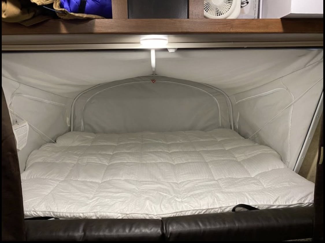 Inside an RV rental: a plush pop-out bed with a white comforter & integrated light. Enjoy comfy sleep on your camper adventure.. Jayco Jay Feather 2017