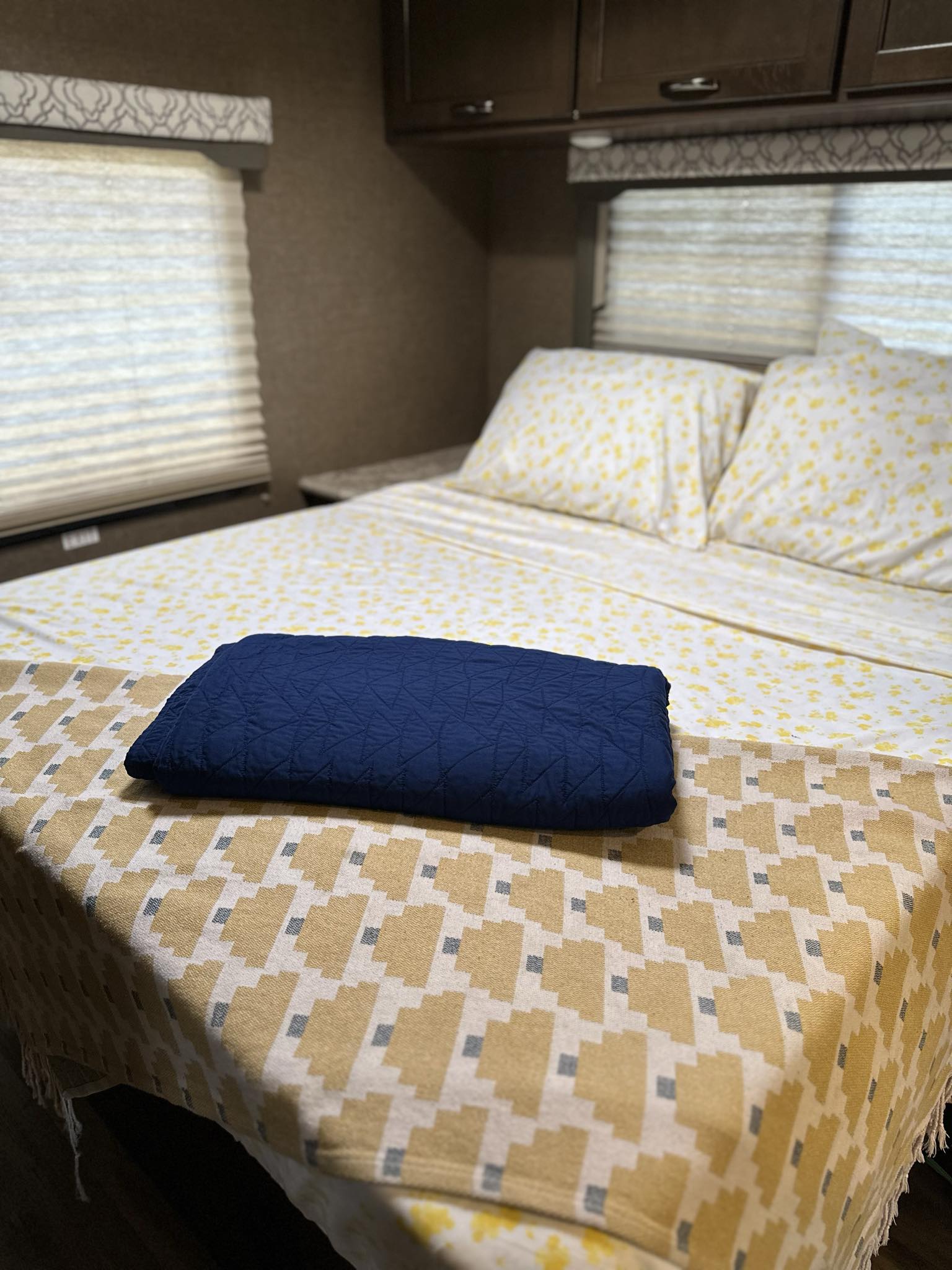 Cozy RV rental bedroom with a bed featuring yellow floral sheets, a blue blanket, and a patterned throw.. Thor Motor Coach Freedom Elite 2019