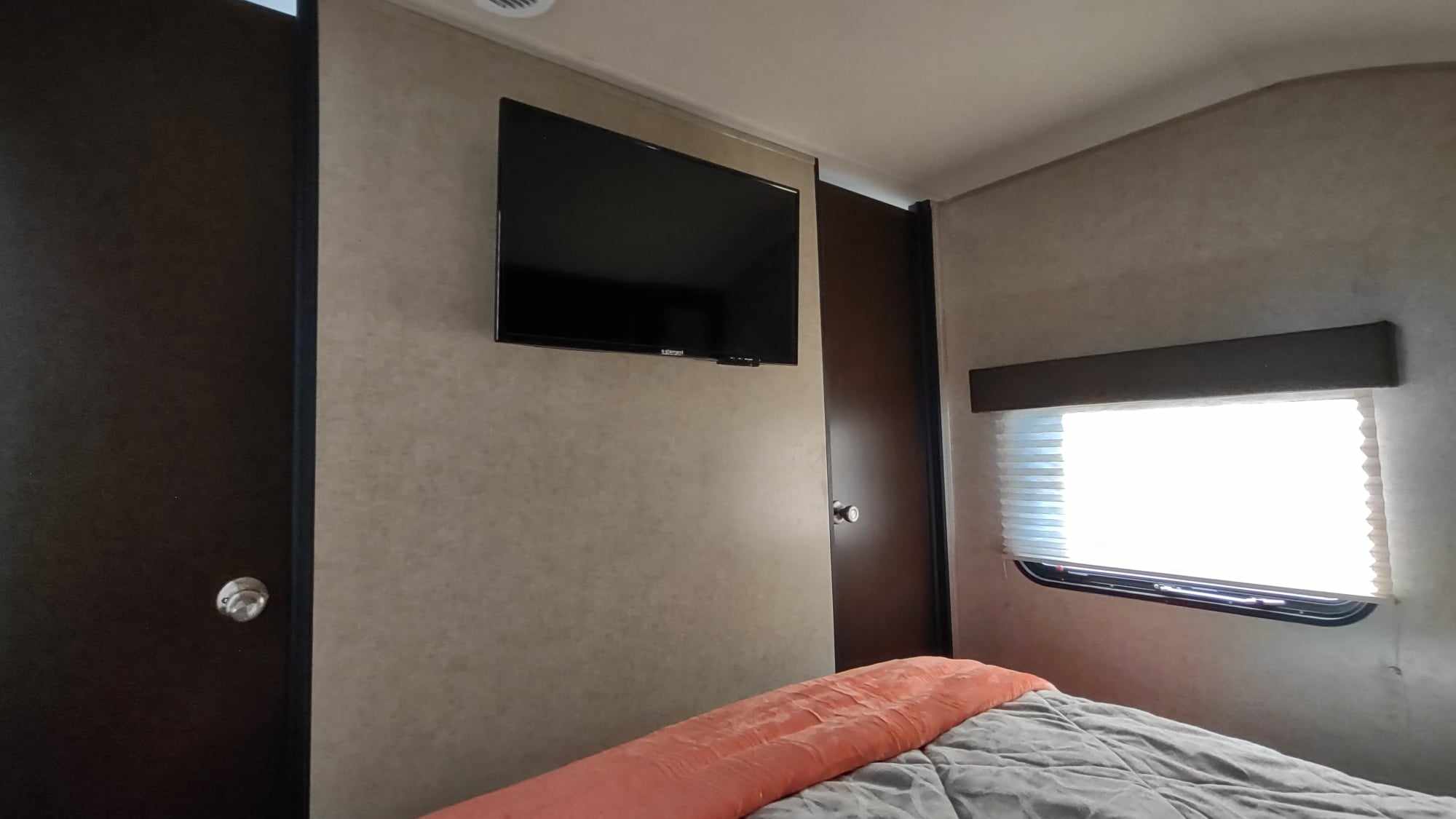 Explore a comfortable RV rental bedroom featuring a wall-mounted TV, cozy bed, and window with blinds.. Forest River Cherokee 2017
