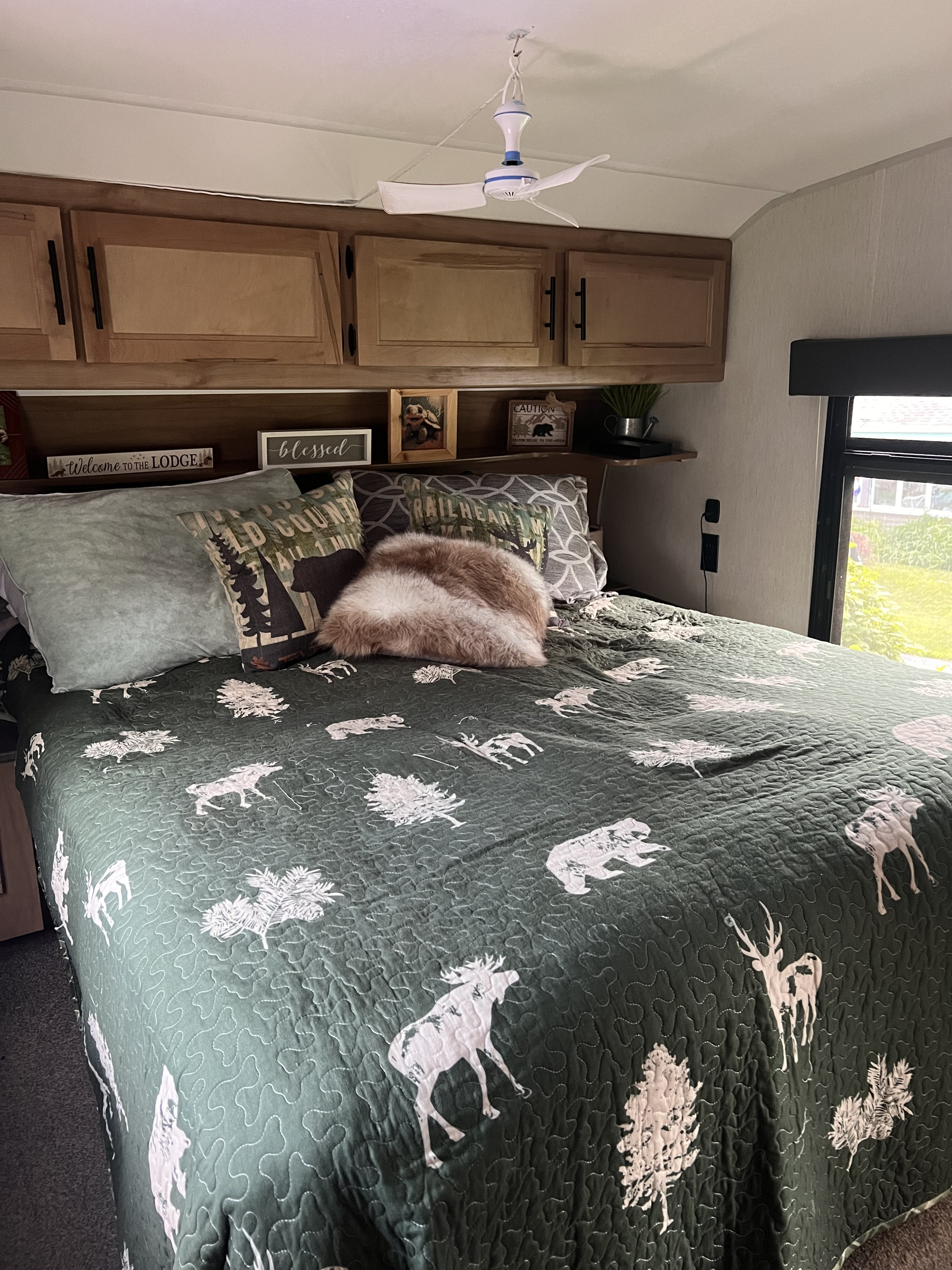 Cozy RV rental bedroom features lodge-themed decor with a quilted bedspread, pillows, overhead cabinets, and a ceiling fan.. Forest River Cherokee Cherokee Black Label Series 2023