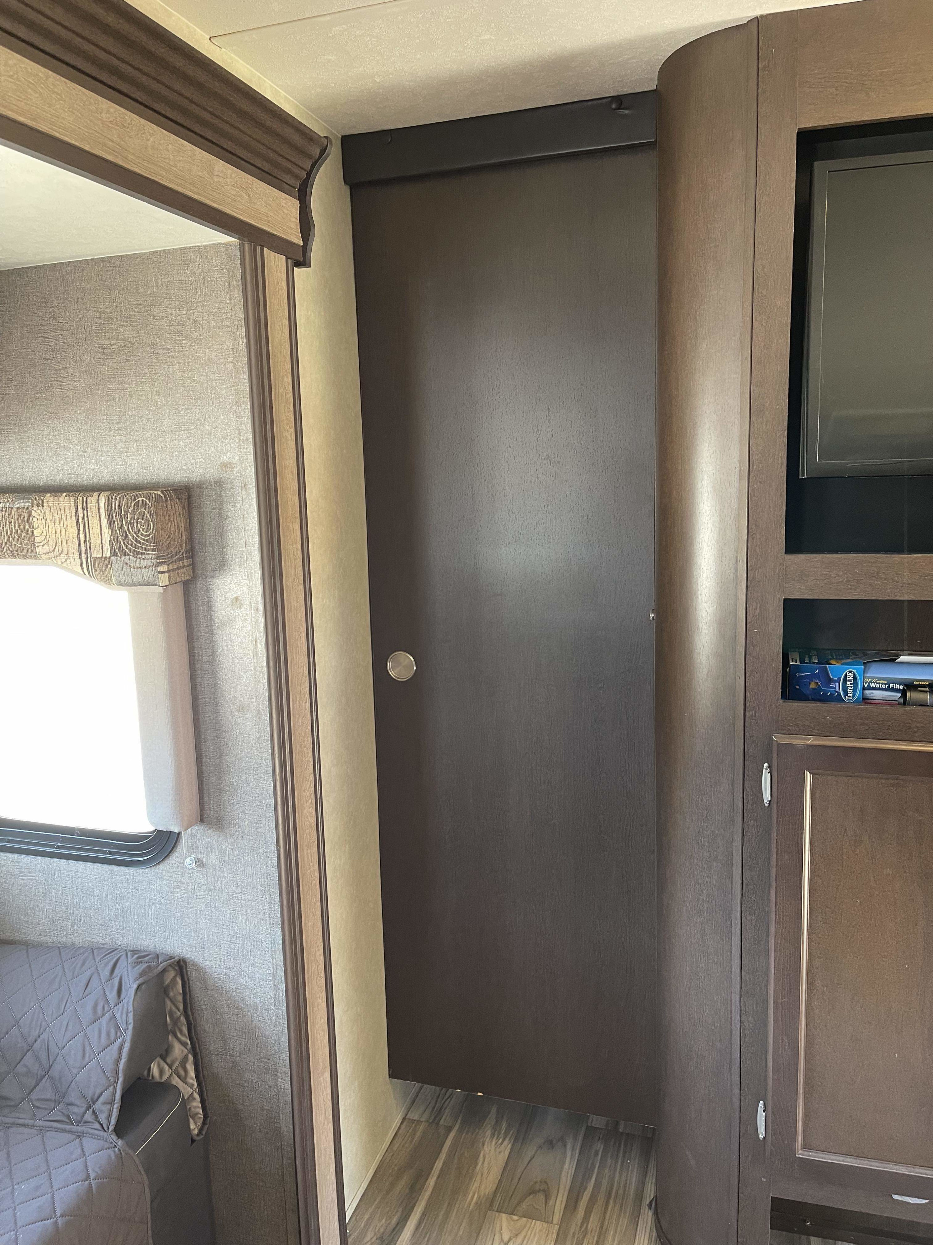 RV rental interior featuring dark wood cabinetry with a TV, a closed door, and a window with a patterned valance.. Forest River T2850 2017