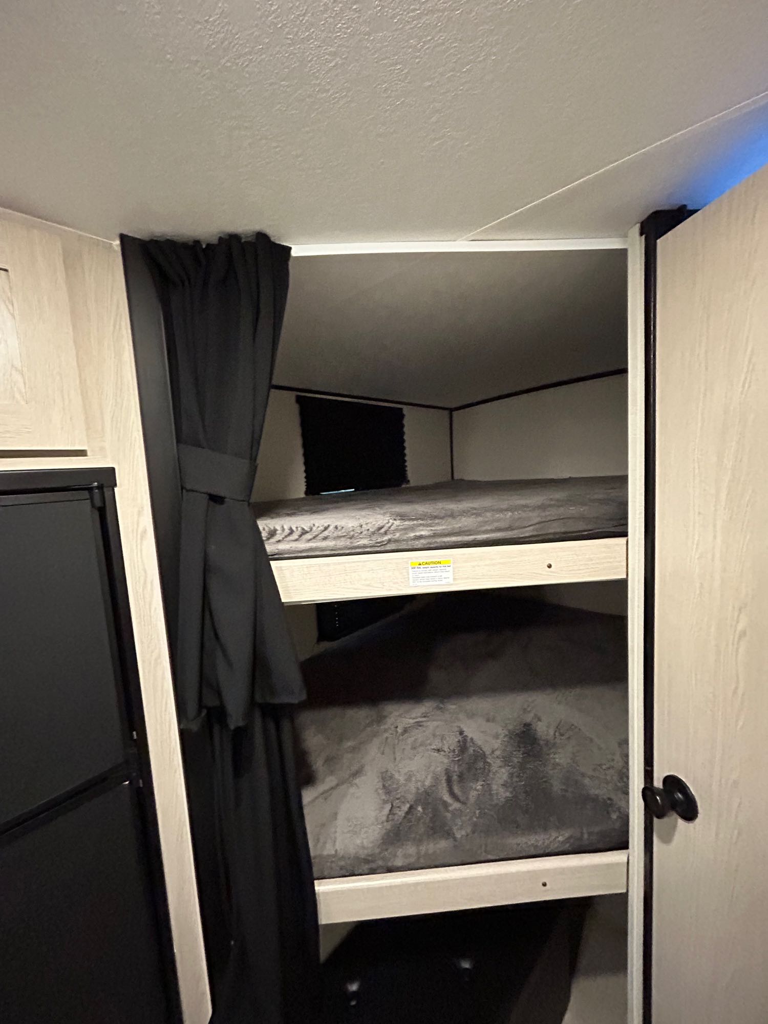 Inside an RV rental: dark bunk beds with privacy curtain and a fridge nearby. Compact living space for travel.. Coachmen Apex Nano 2021