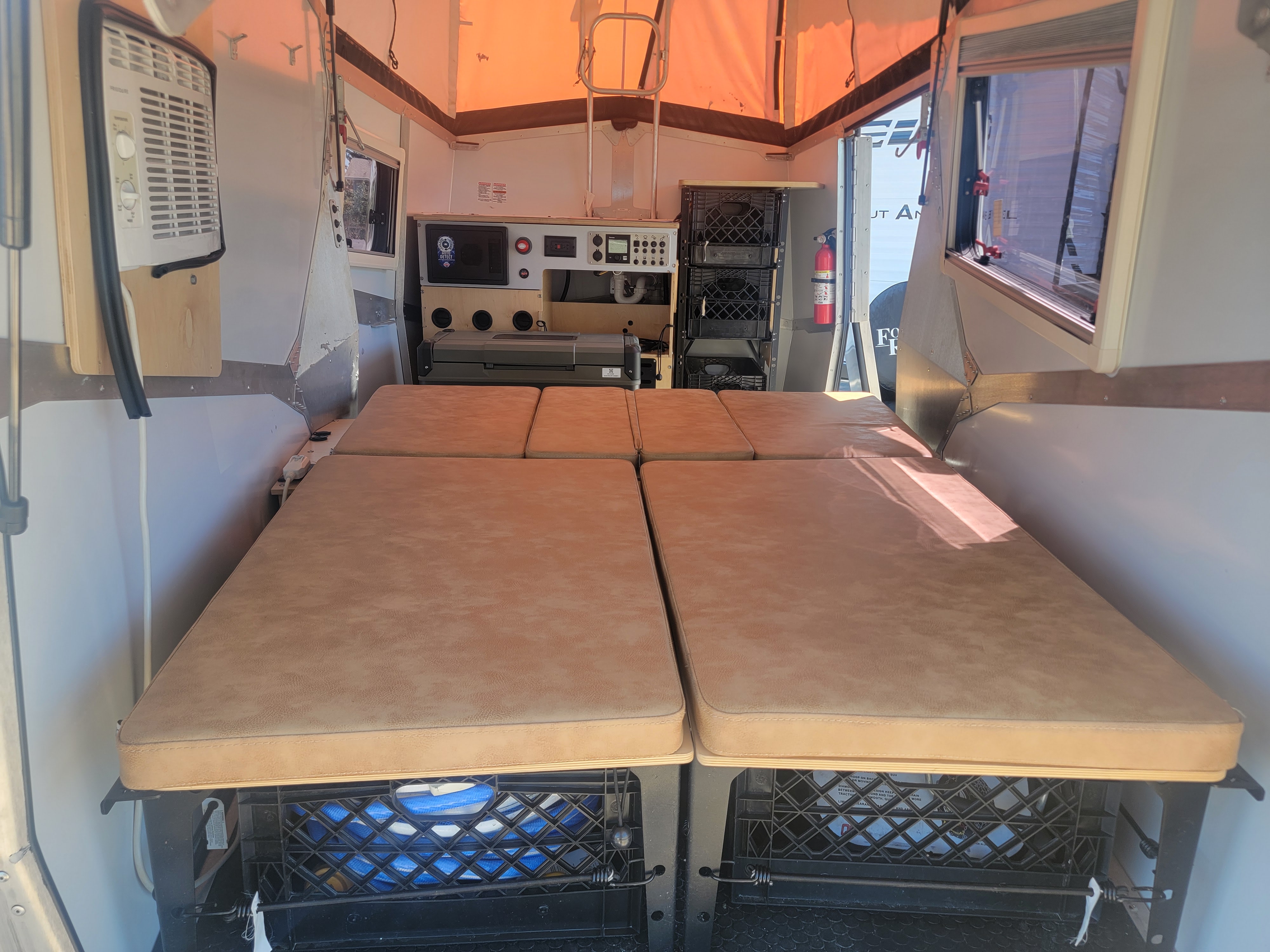 Step inside this cozy rv rental interior featuring a versatile bed, under-bed storage crates, AC unit, and control panel.. TAXA OUTDOORS CRICKET 2023