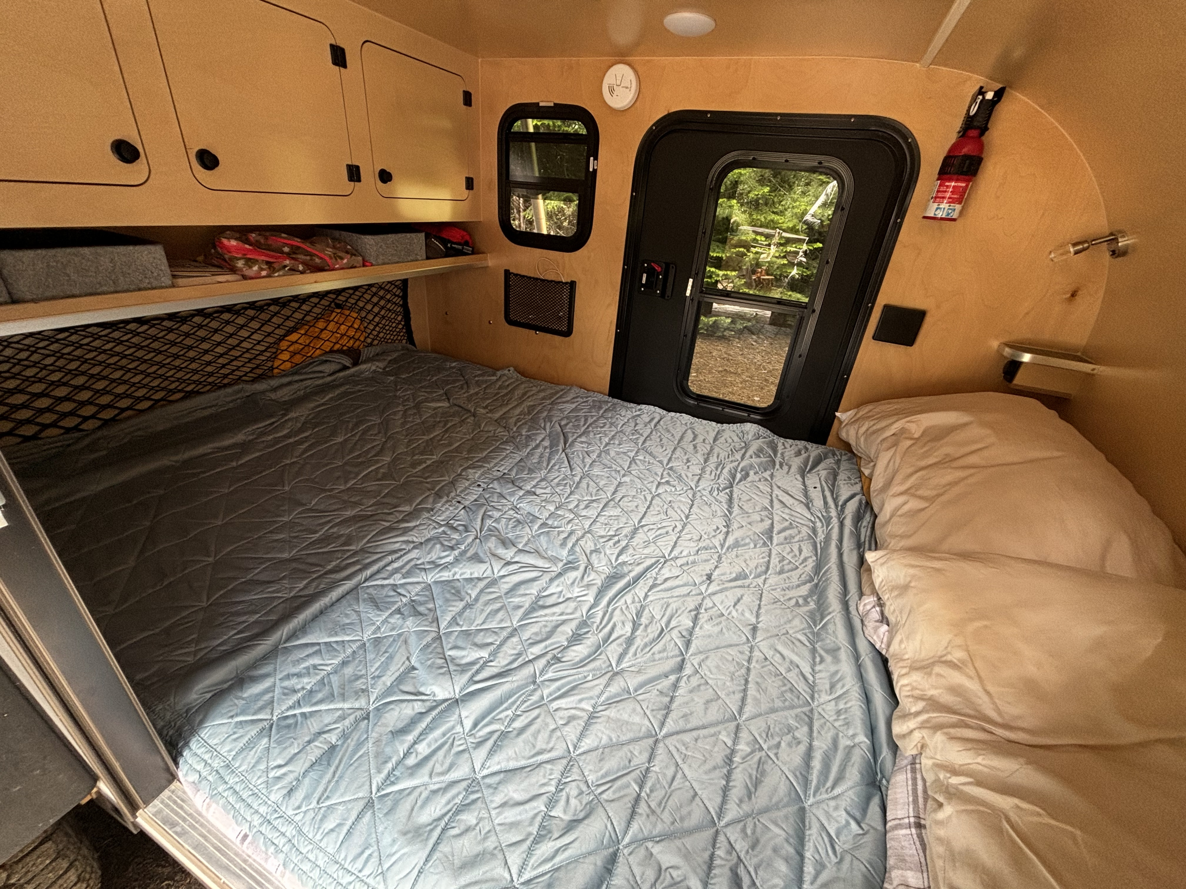 Cozy RV rental bedroom with a large quilted bed, overhead storage, and a window to nature.. Aero Teardrops Burnside 2024