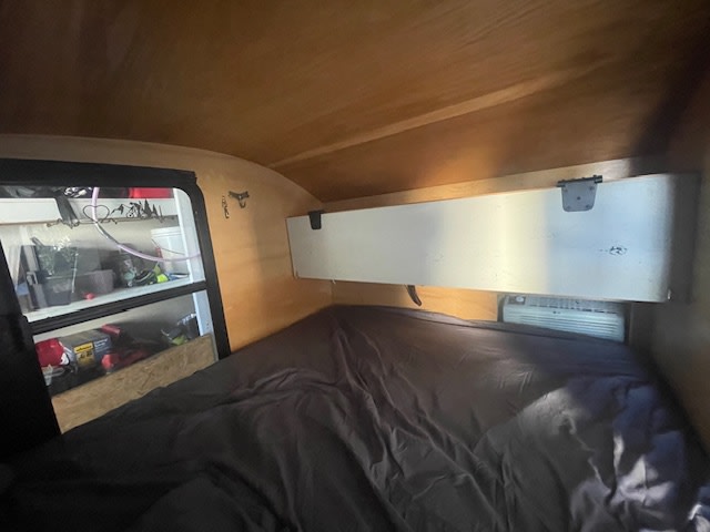 Inside an RV rental: a compact sleeping area with a bed, AC unit, and side window showing outside storage.. Custom Built Teardrop 2014