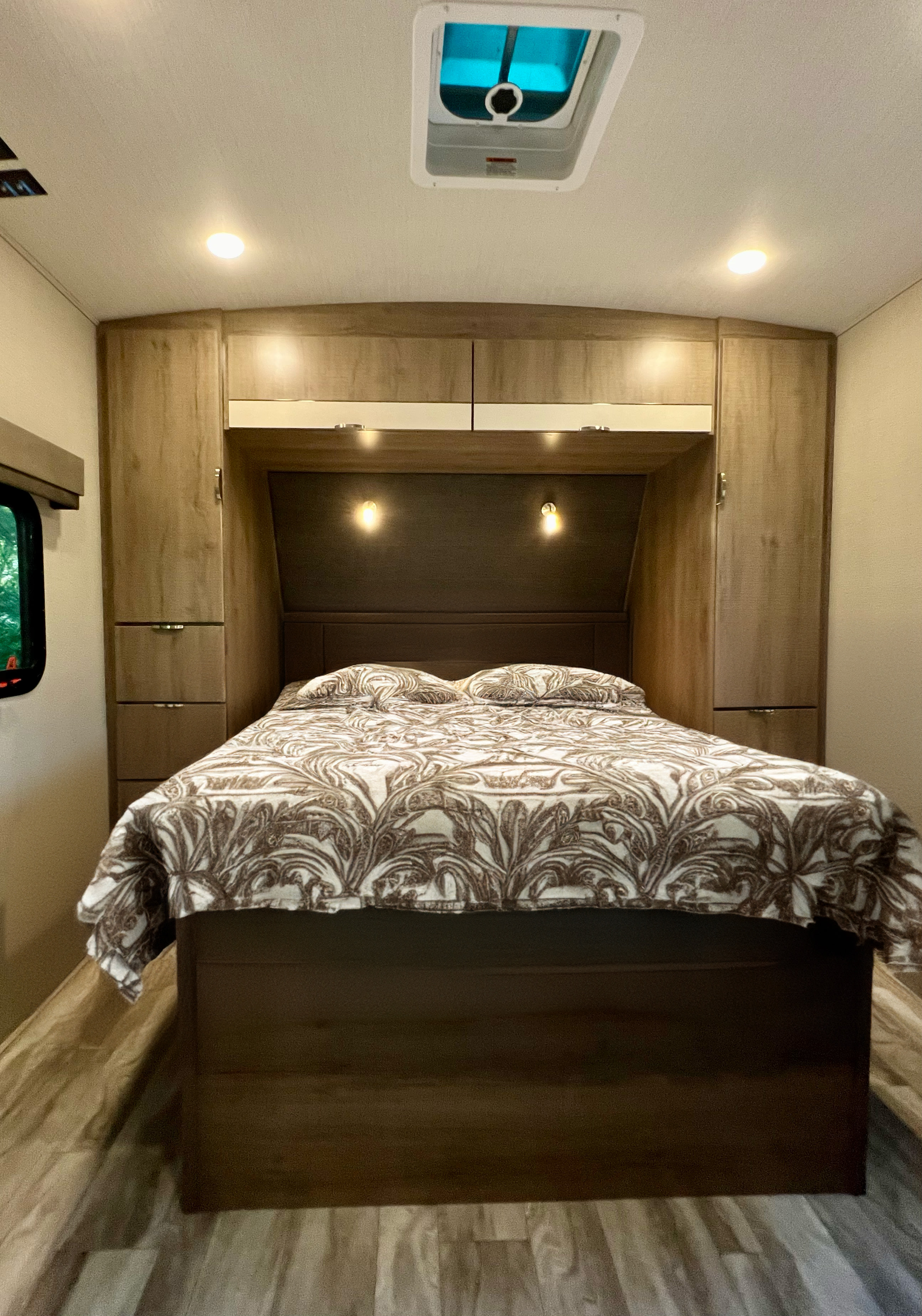 Cozy RV rental bedroom features a patterned bed, built-in storage, overhead cabinets, and a skylight for natural light.. Grand Design Imagine 2020