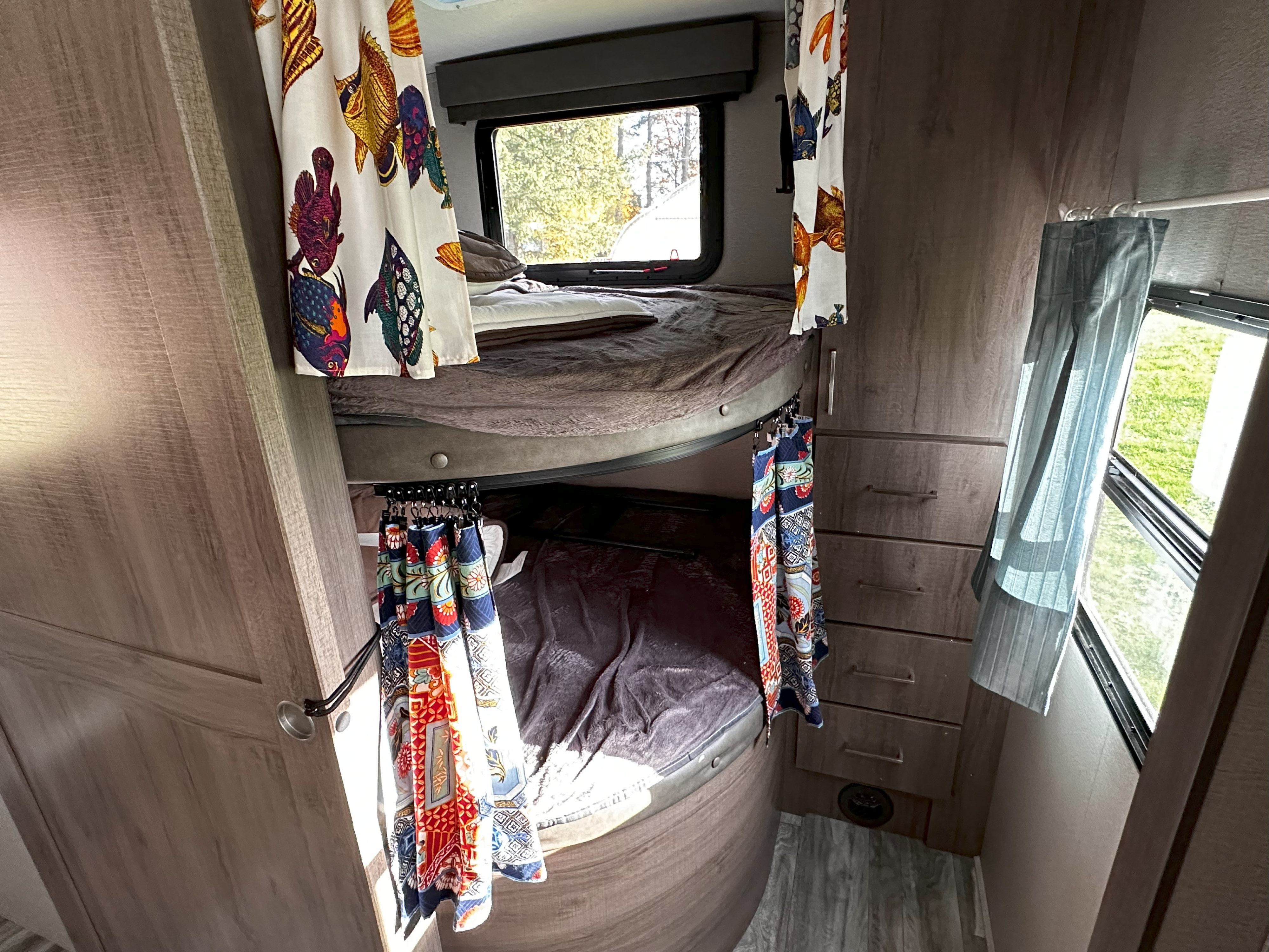 Colorful bunk beds with privacy curtains inside an RV rental, offering cozy sleeping space with a view.. Grand Design Imagine 2022