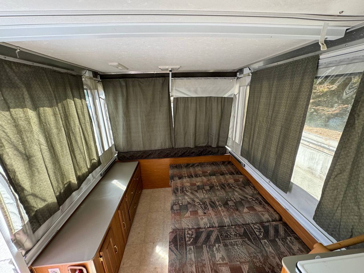 View inside an RV rental pop-up camper, showing comfortable beds, bright windows with privacy curtains, and storage.. Fleetwood Santa Fe 2004