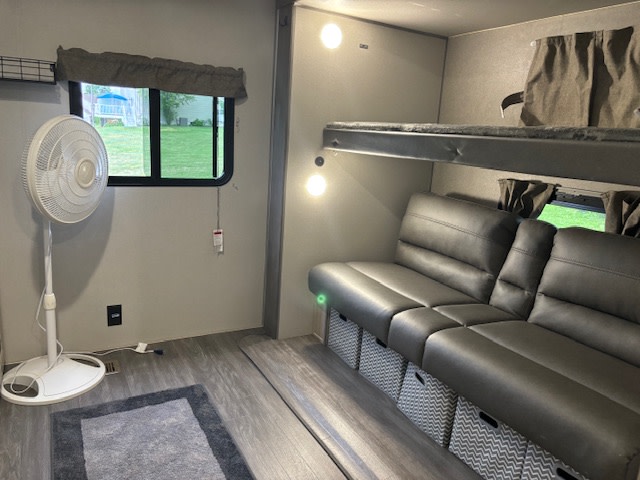 Cozy RV rental interior with bunk beds, a gray couch with storage, and a fan by the window, offering a comfortable living space.. Forest River Aurora Aurora 2024